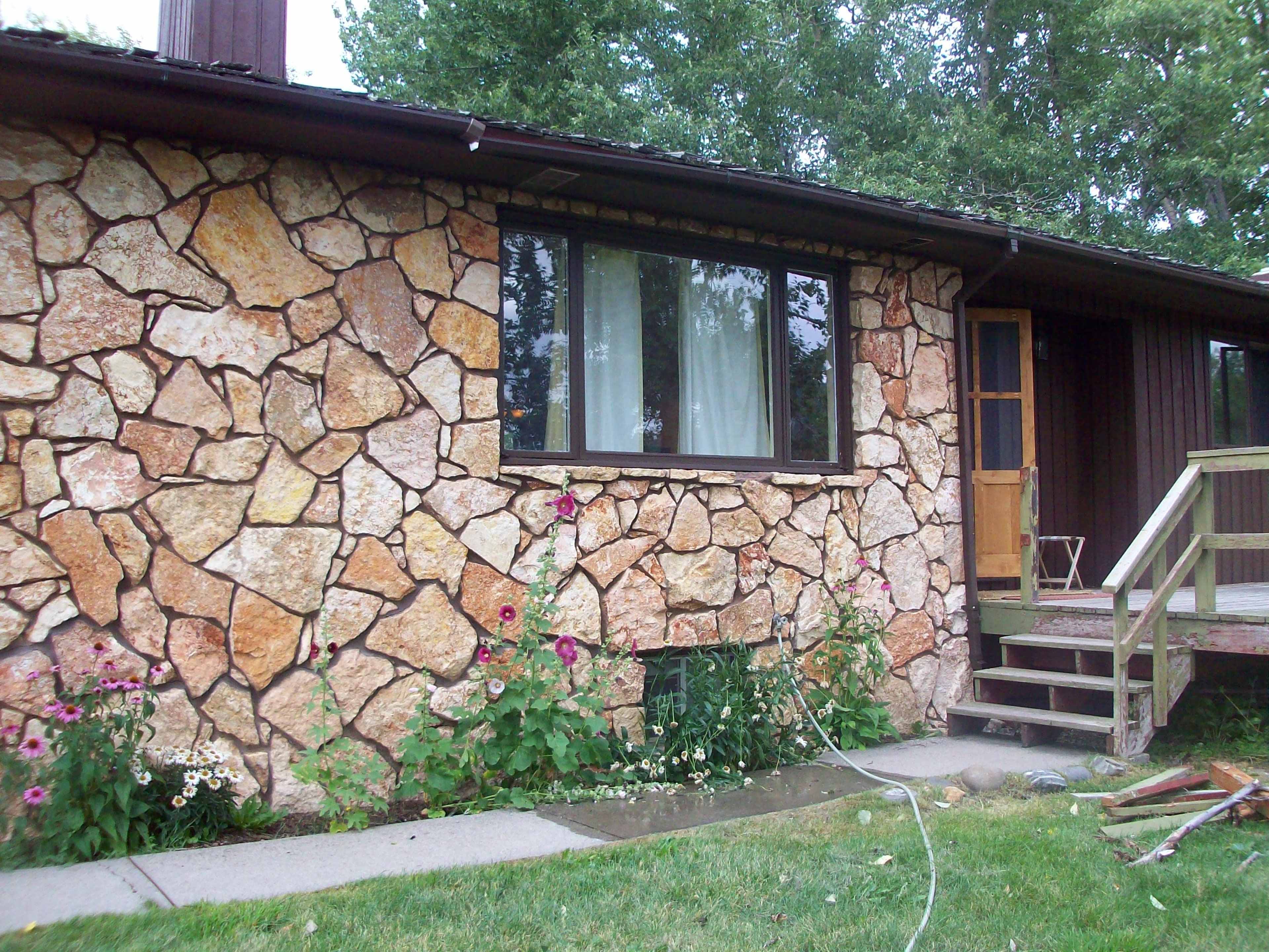 A house with a stone exterior, a large window, and a wooden front door beside a small set of stairs leading to the porch.