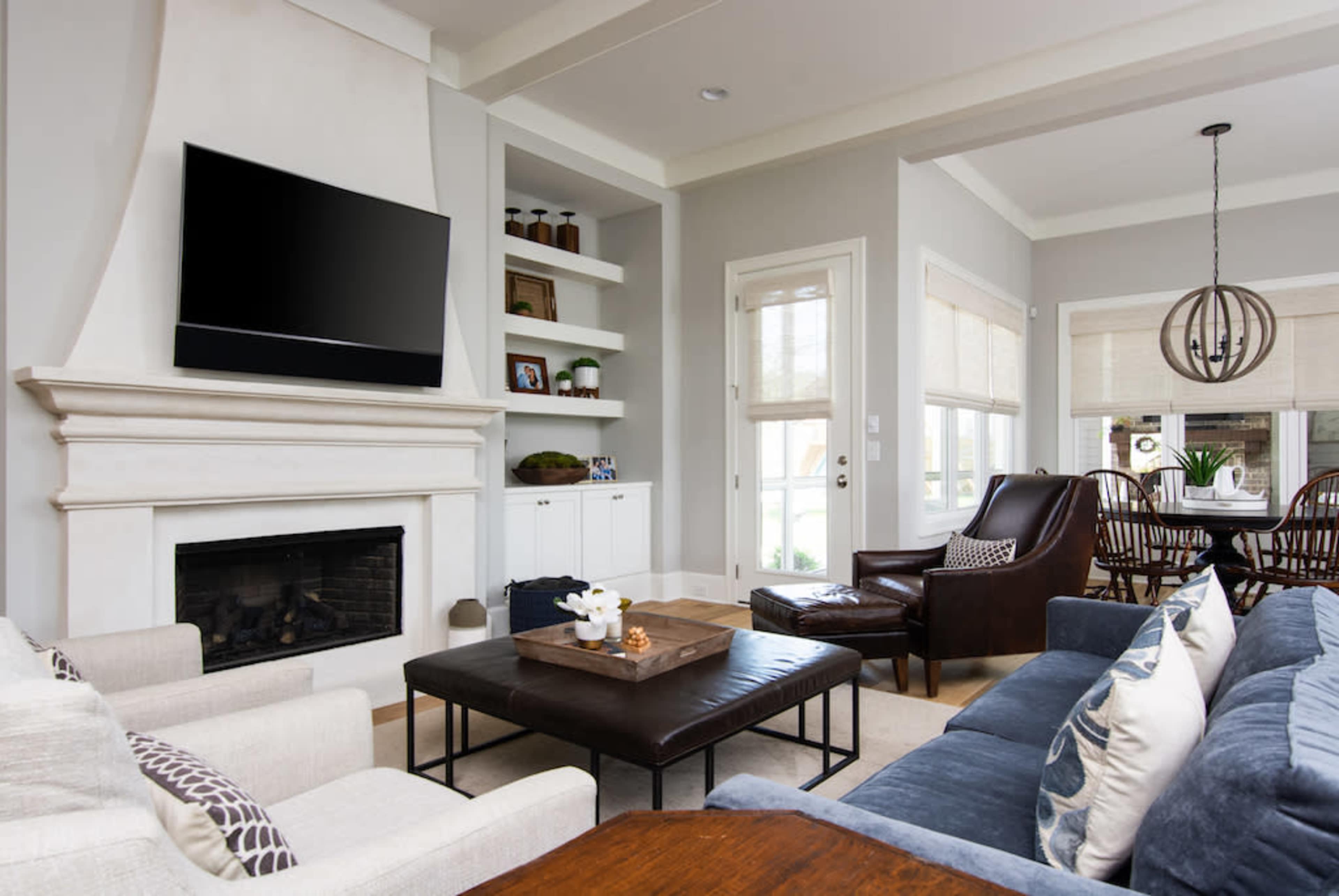 The image shows a modern living room featuring a fireplace, a large coffee table, a sectional sofa, and a combination of decorative shelves and windows.