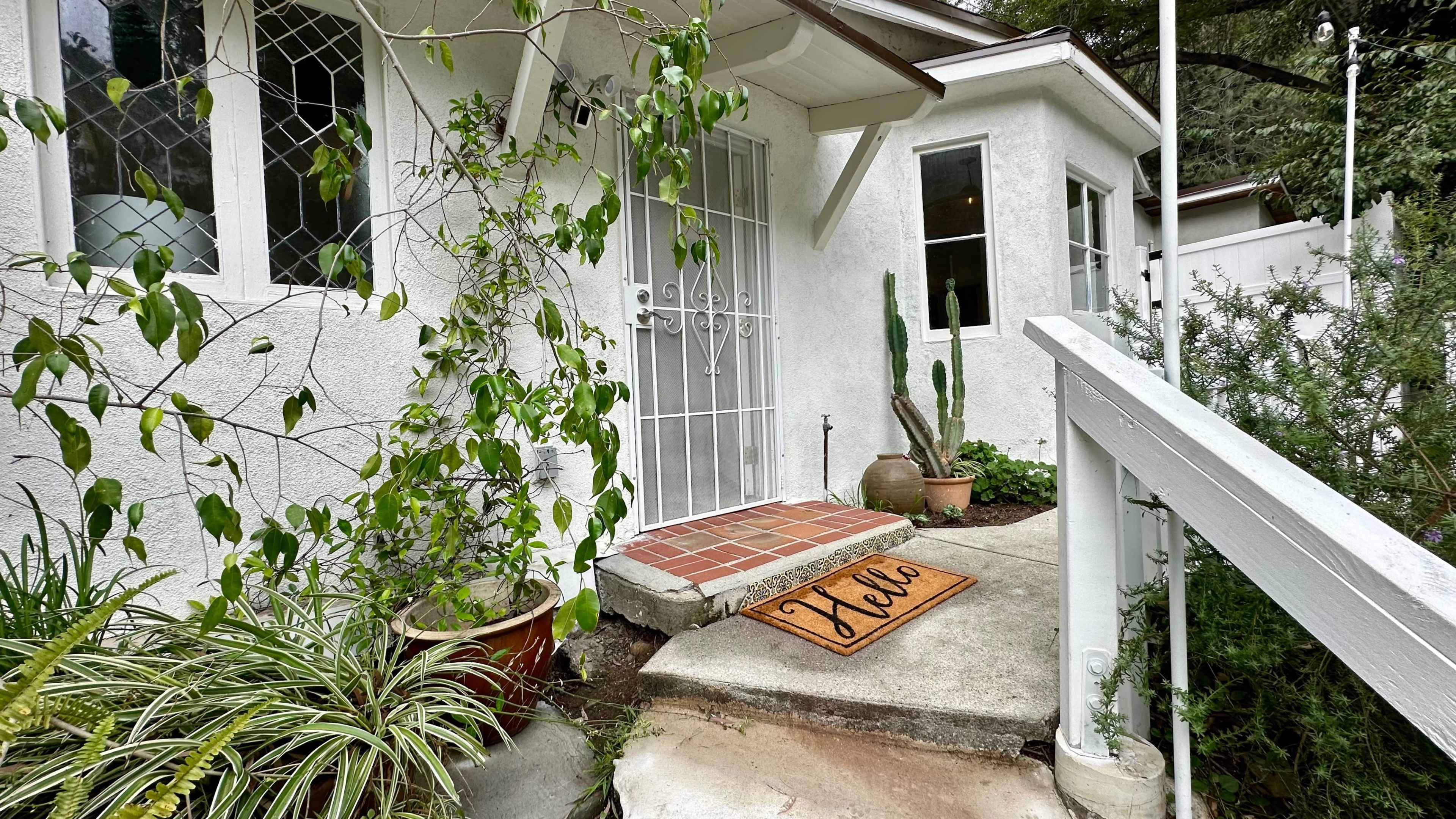 A front entrance to a house is shown, featuring a welcome mat, potted plants, and a metal security door.