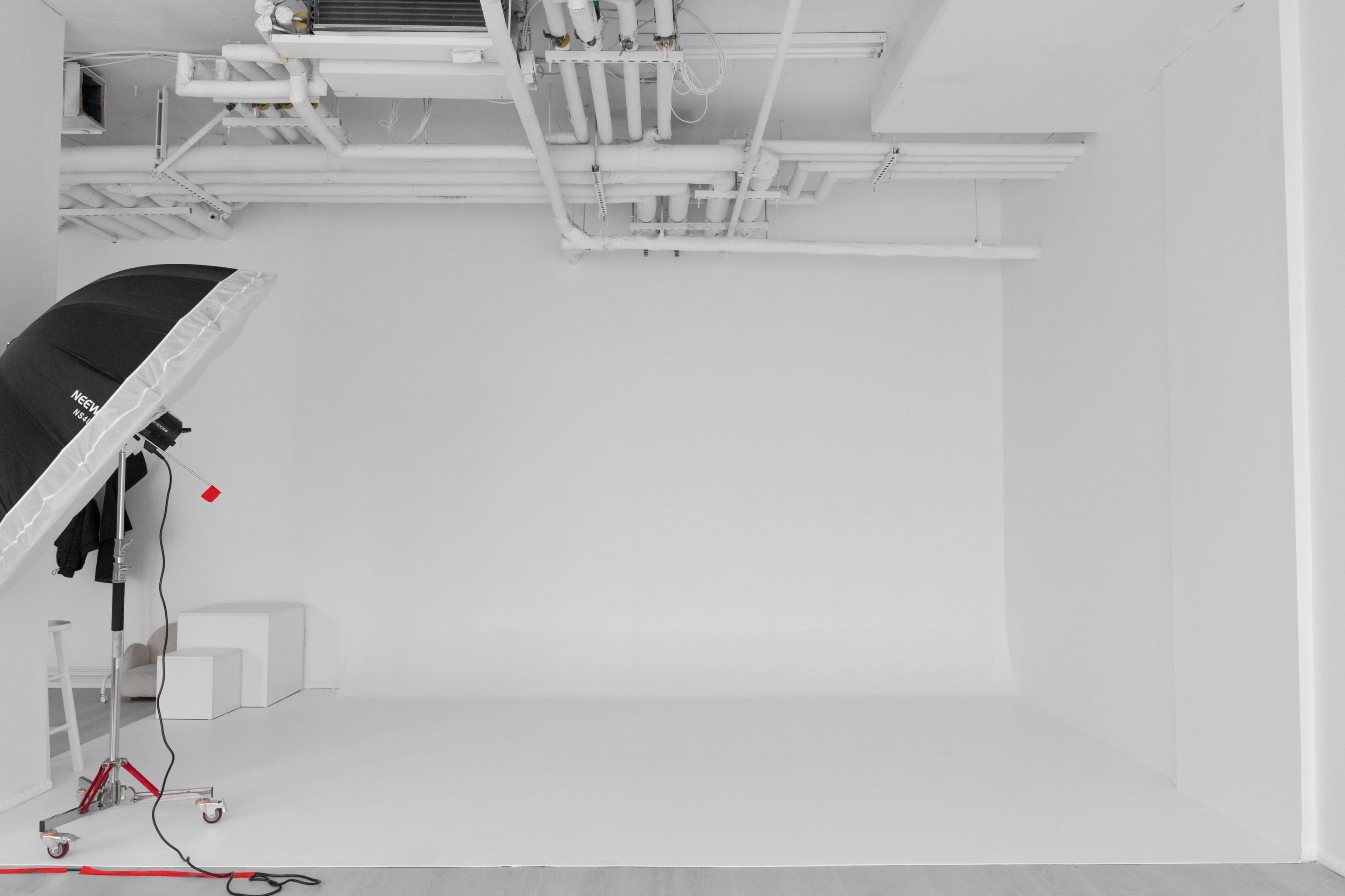 The image shows a minimalist white photography studio with a large softbox light and a few white props.