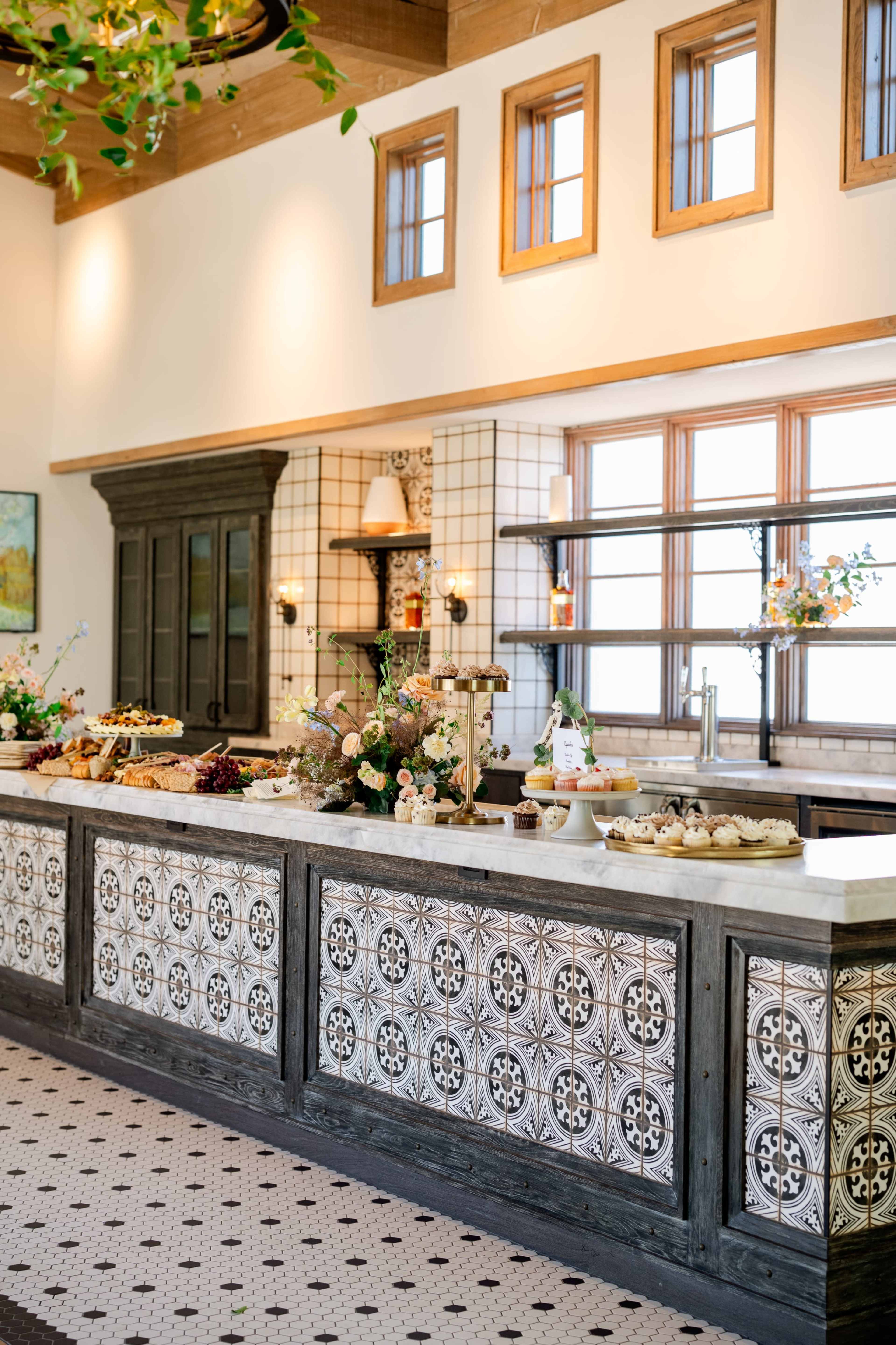 A beautifully designed kitchen with a patterned backsplash, ample natural light from multiple windows, and a countertop filled with various baked goods and decorative flowers.