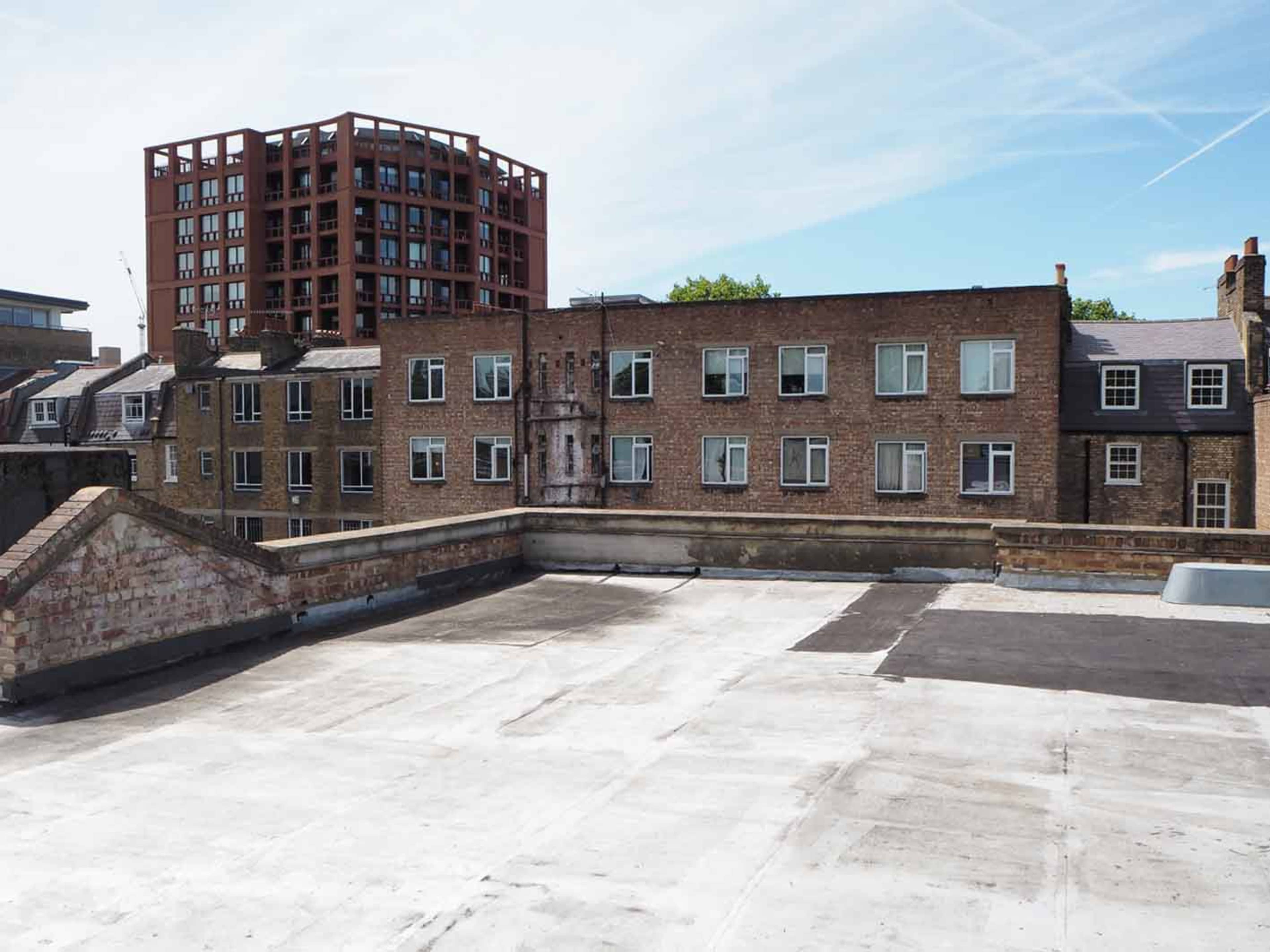 The image shows a flat rooftop with several buildings in the background, including a brick structure and a taller red building.