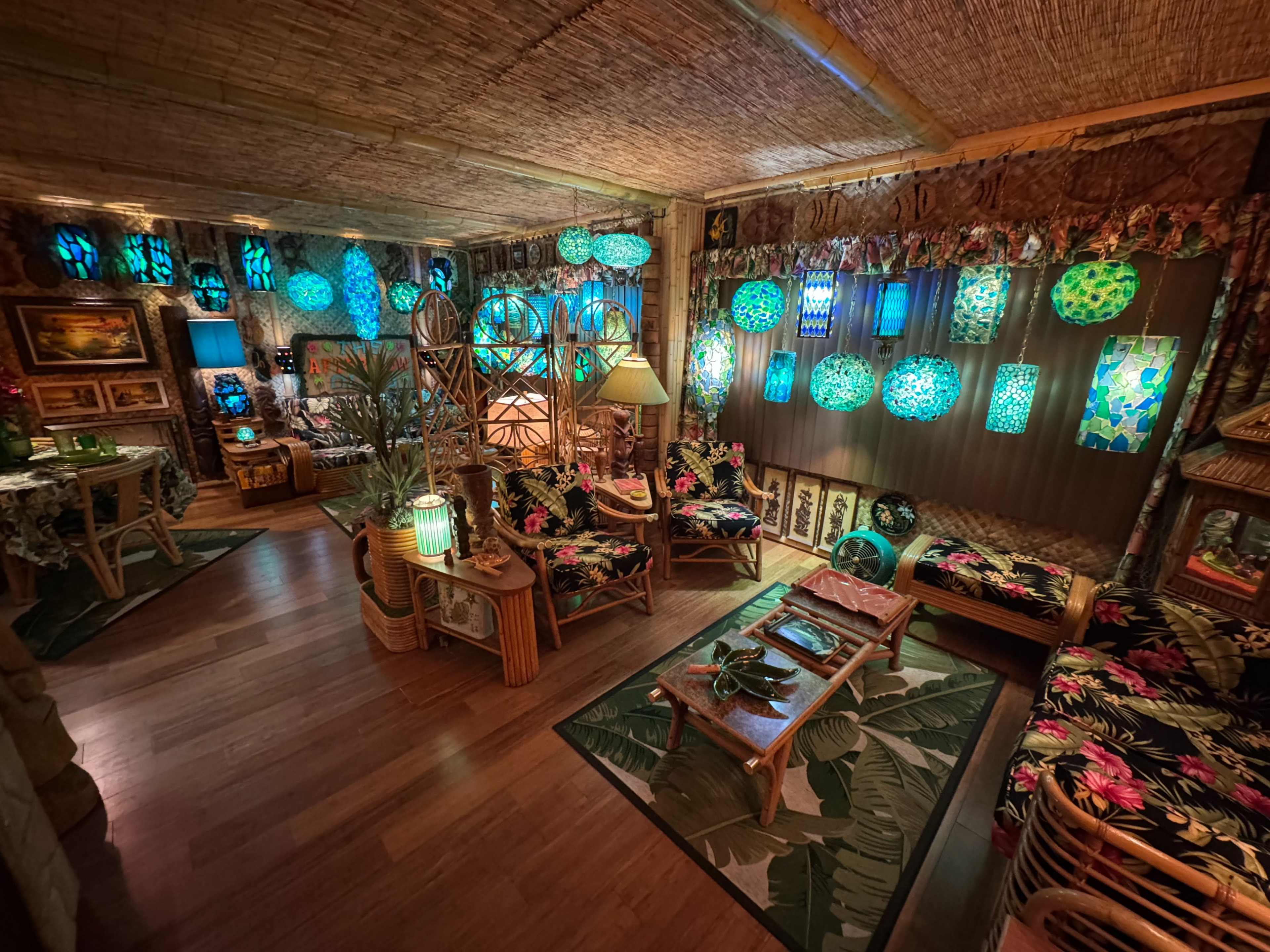 The image shows a decorated room with tropical-themed furniture, vibrant light fixtures, and green-blue accent lighting.