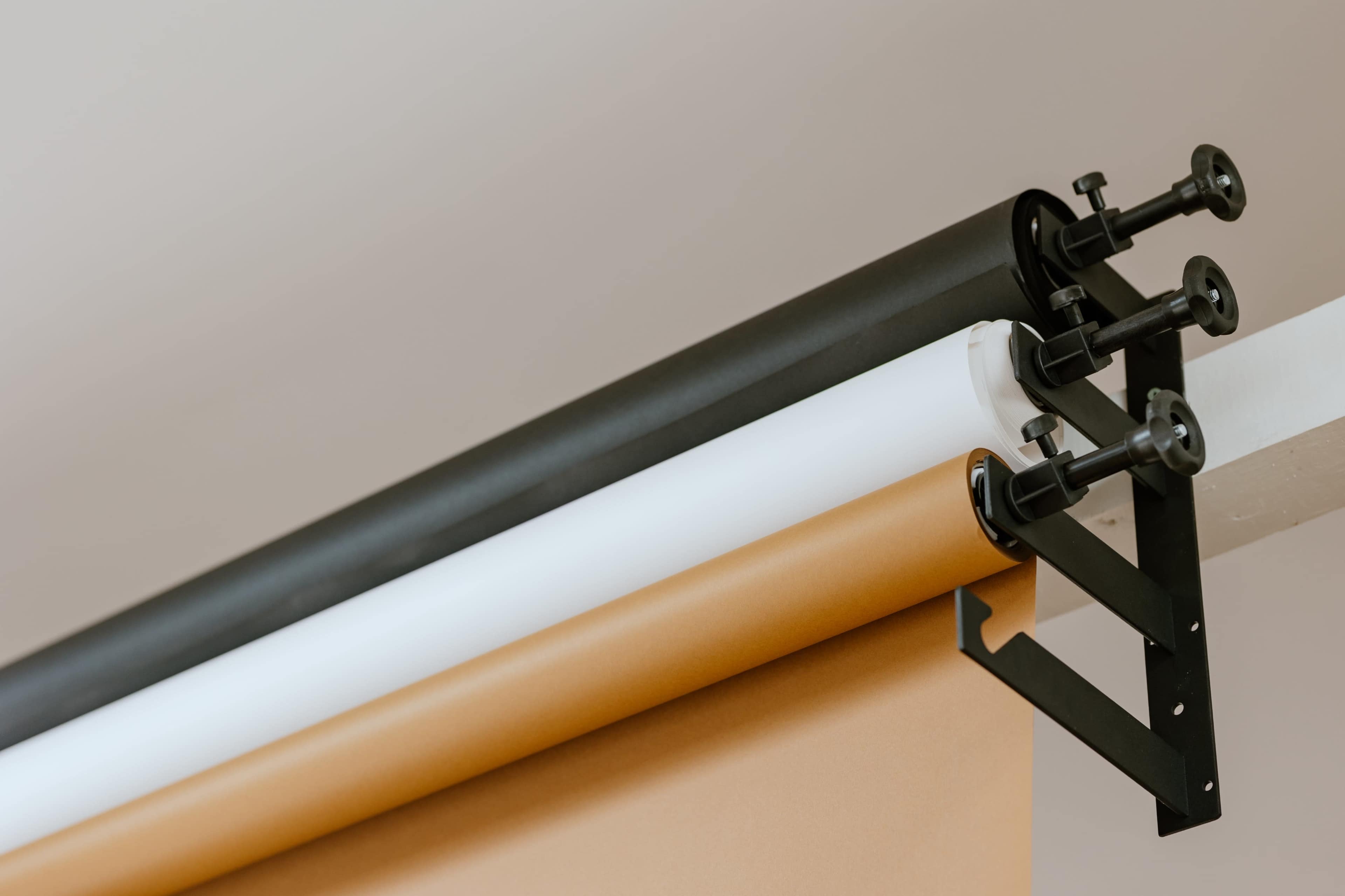 The image shows a roll of backdrop paper in black, white, and brown, mounted on a support system.