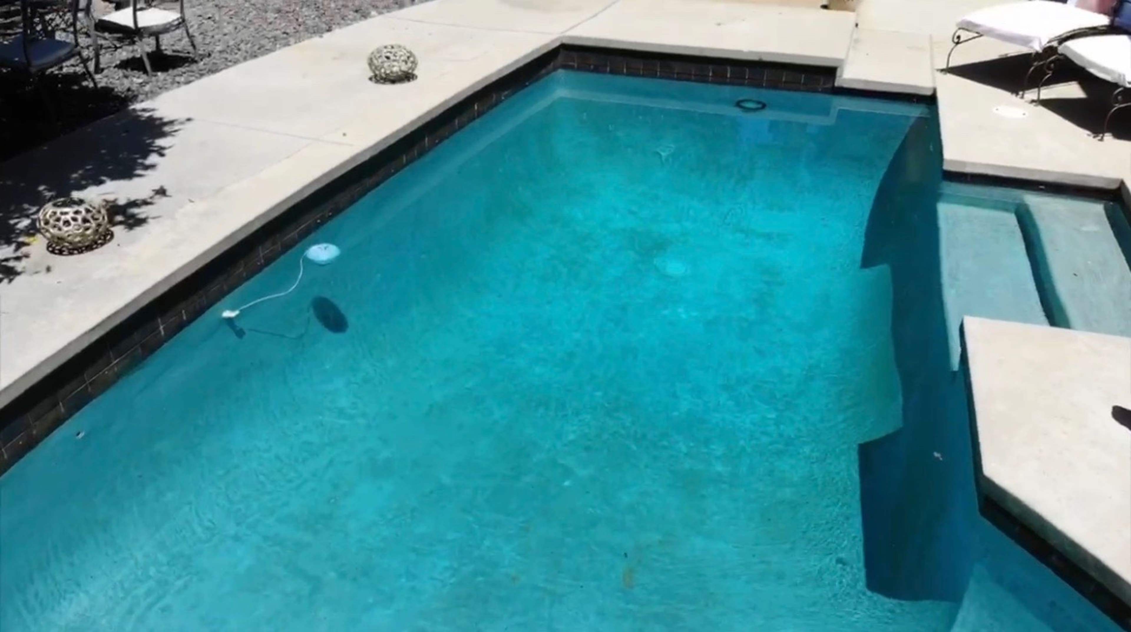 A clear blue swimming pool with steps leading down into the water and a smooth concrete deck surrounding it.