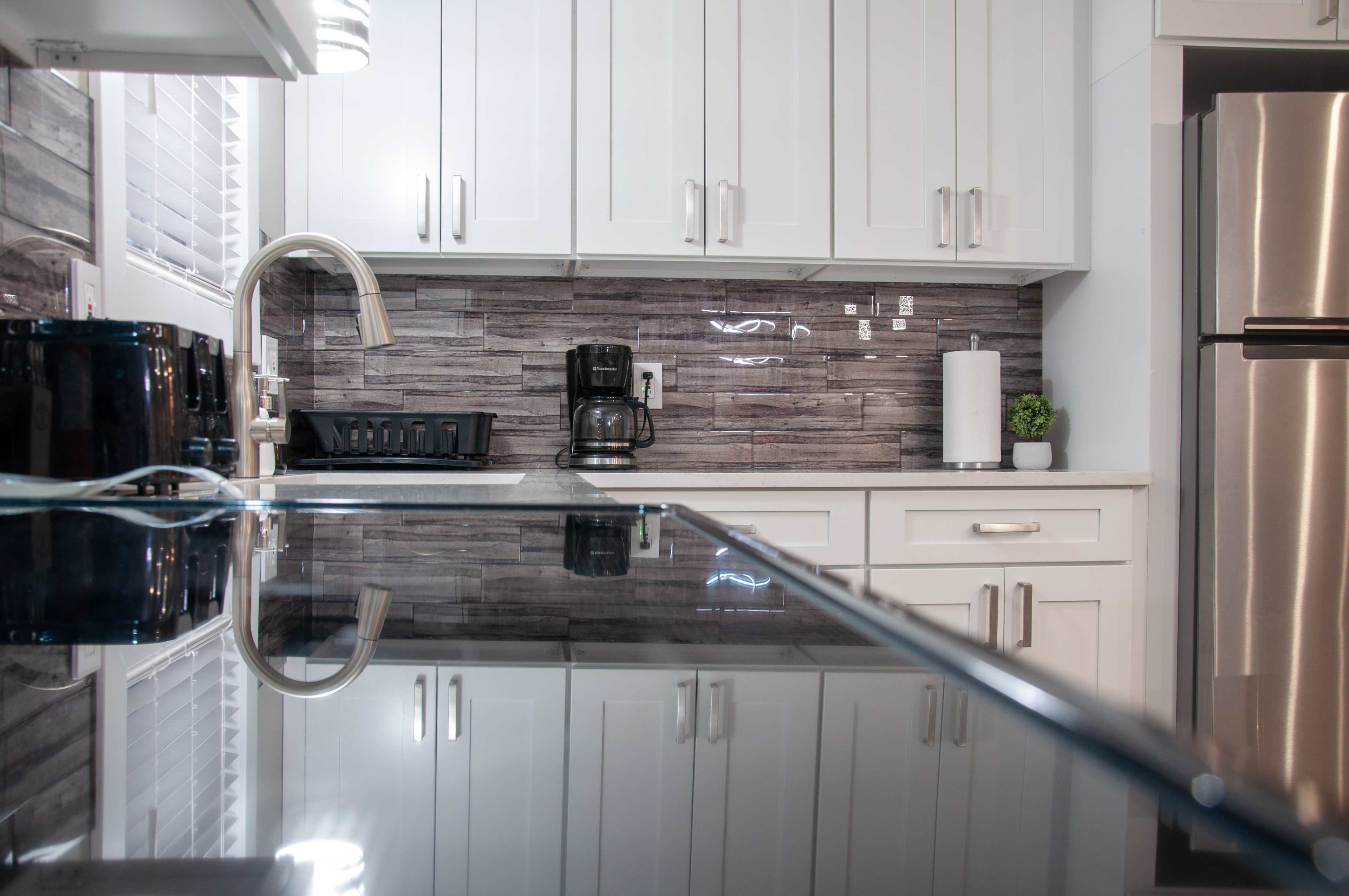 A modern kitchen with white cabinetry, a countertop, and appliances, including a coffee maker and a stainless steel refrigerator.