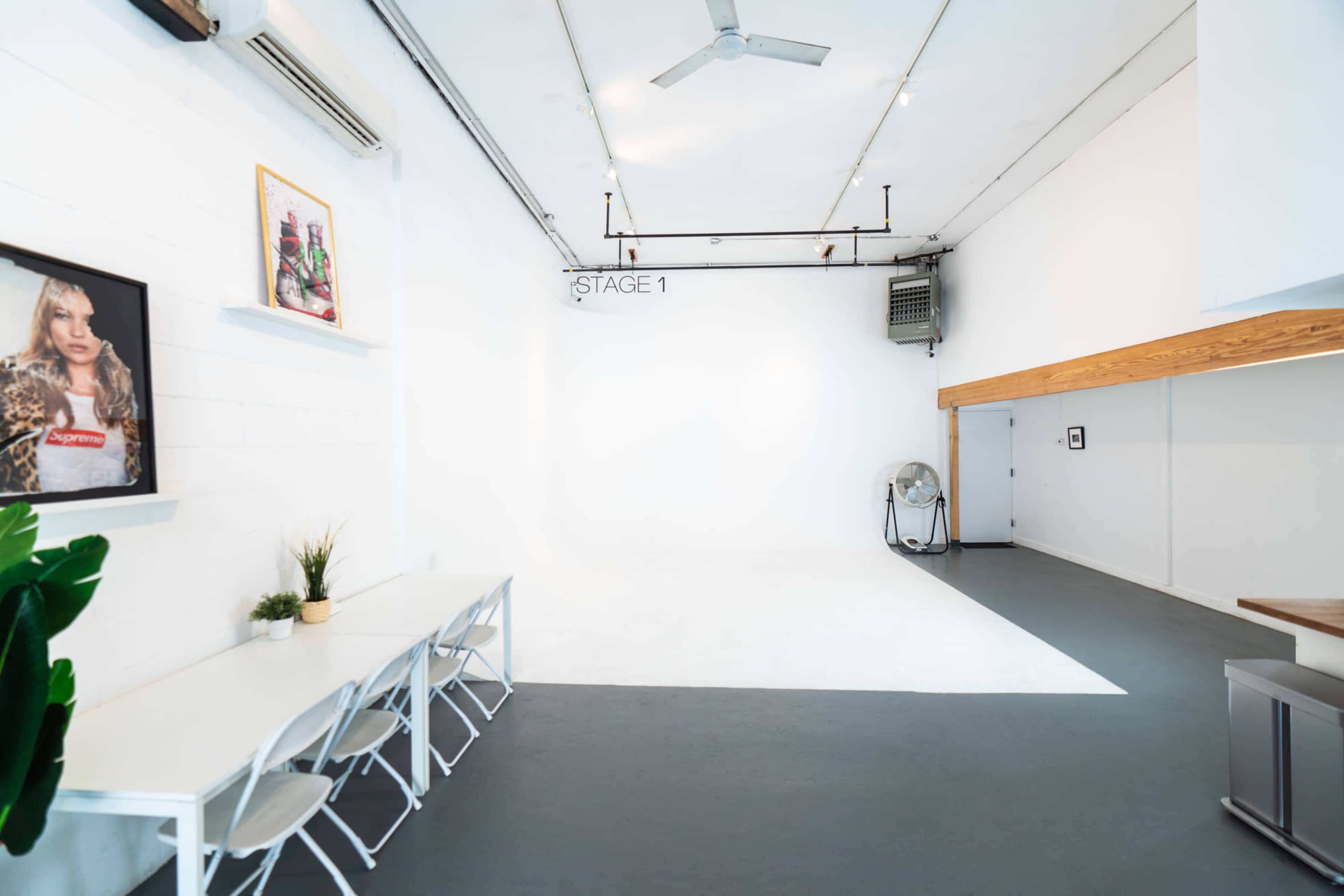 A spacious, well-lit studio with a white backdrop, a fan, a wooden counter, and a table with chairs.