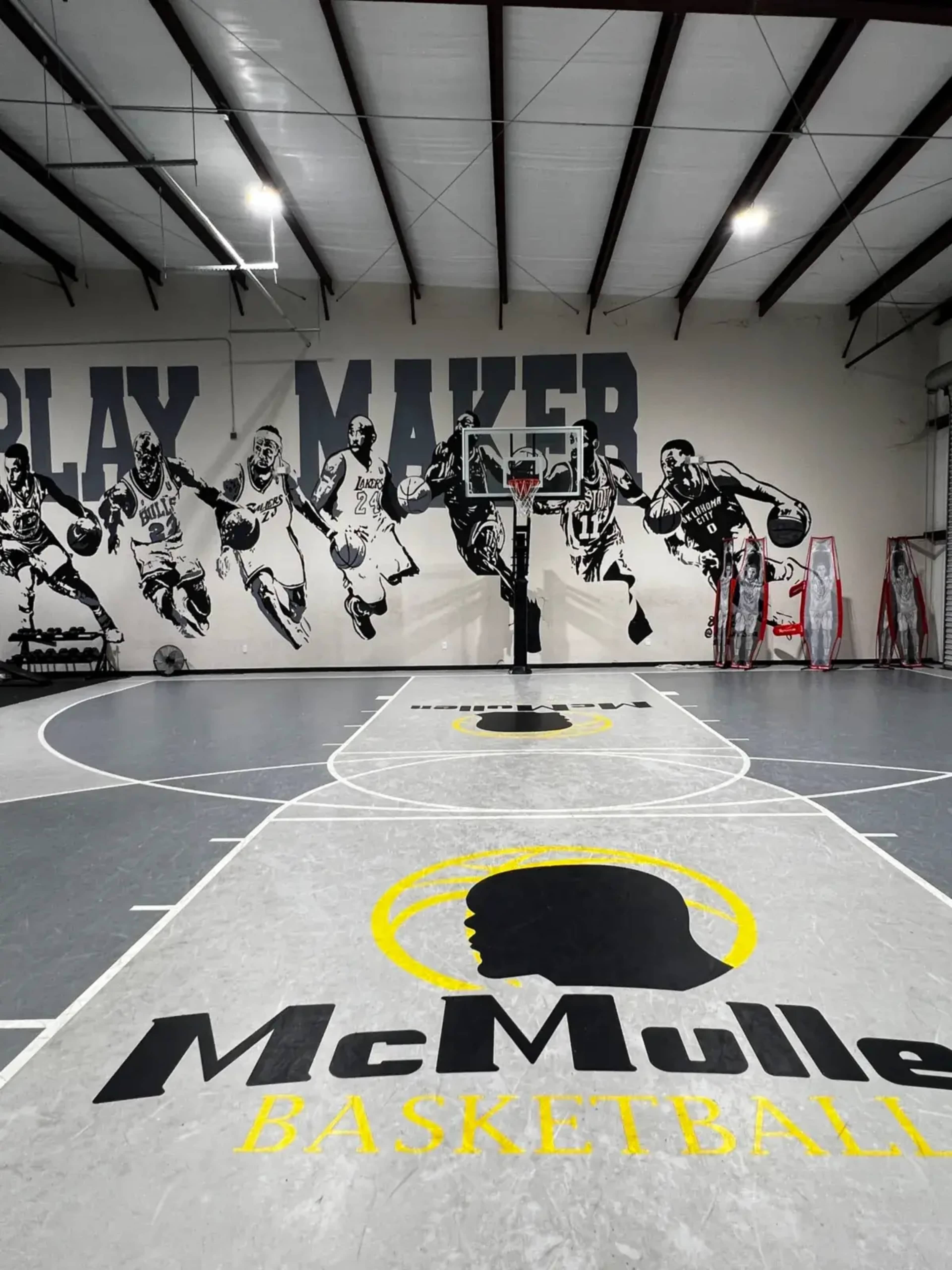 The image shows an indoor basketball court with a large mural of players on the wall and a prominently displayed logo for "McMullen Basketball."