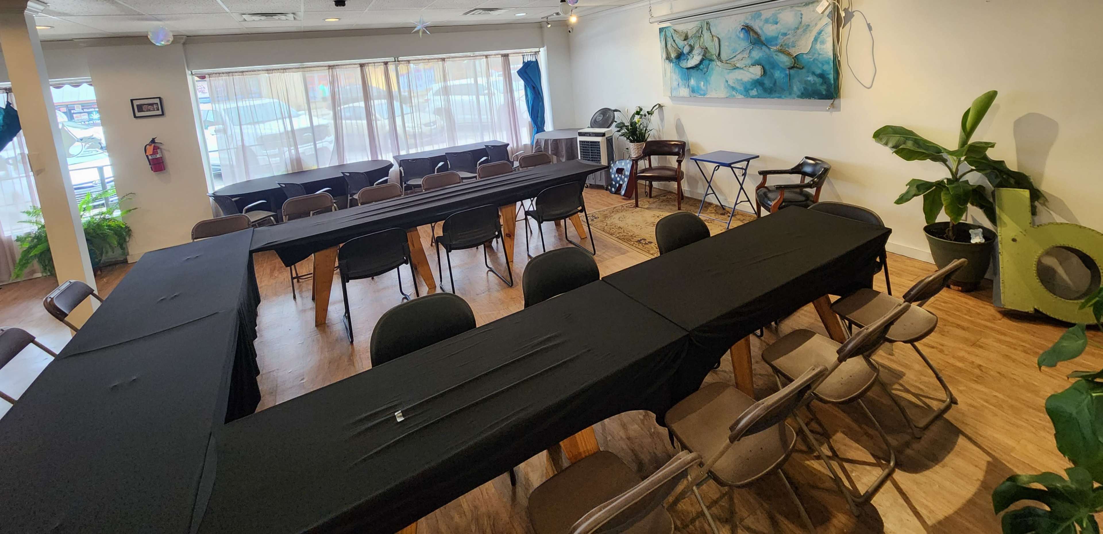 The image shows a meeting room arranged with several tables covered in black tablecloths, set up in a U-shape with chairs placed around them.