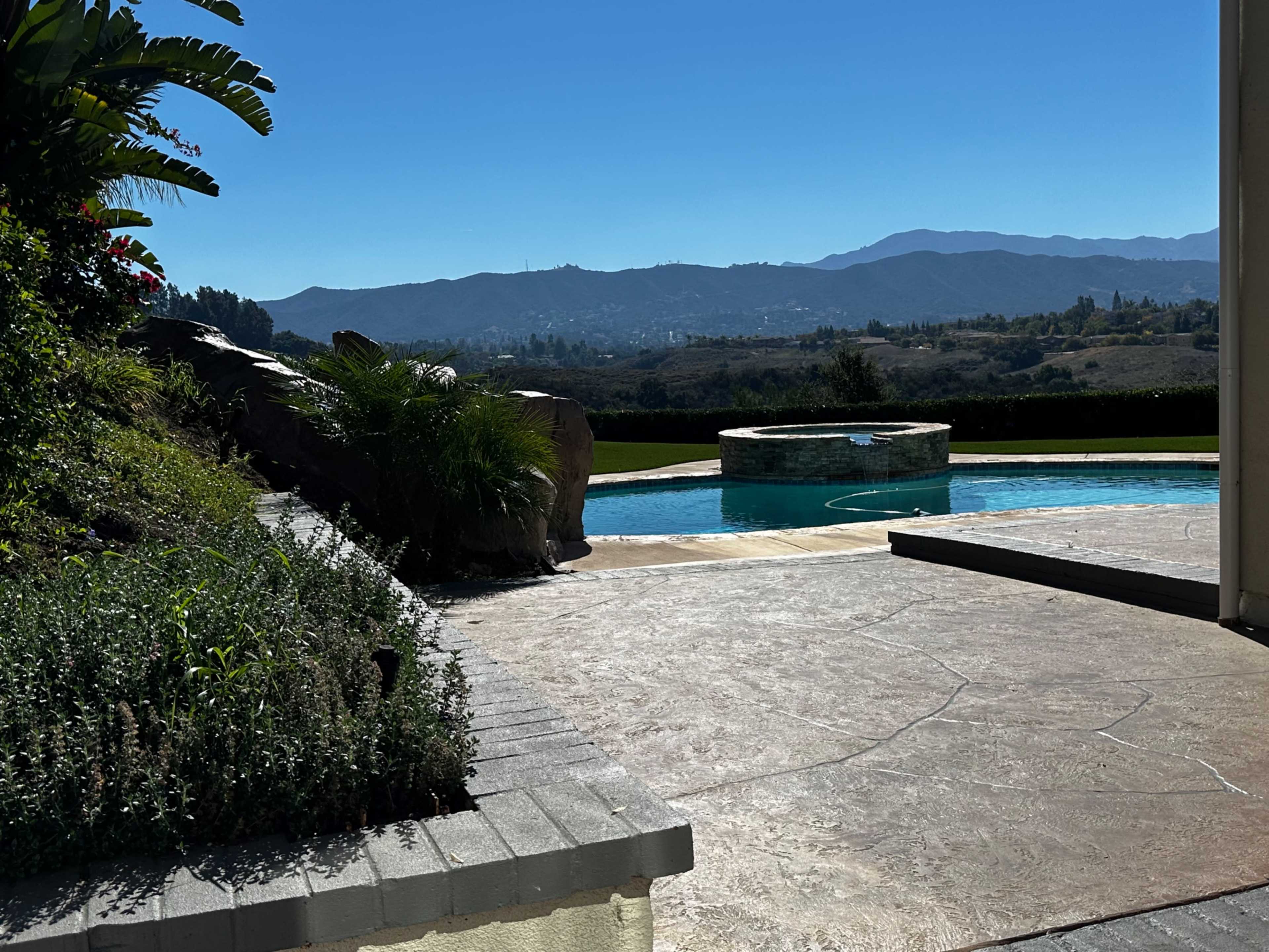A clear view of a swimming pool surrounded by landscaped greenery and mountains in the background.