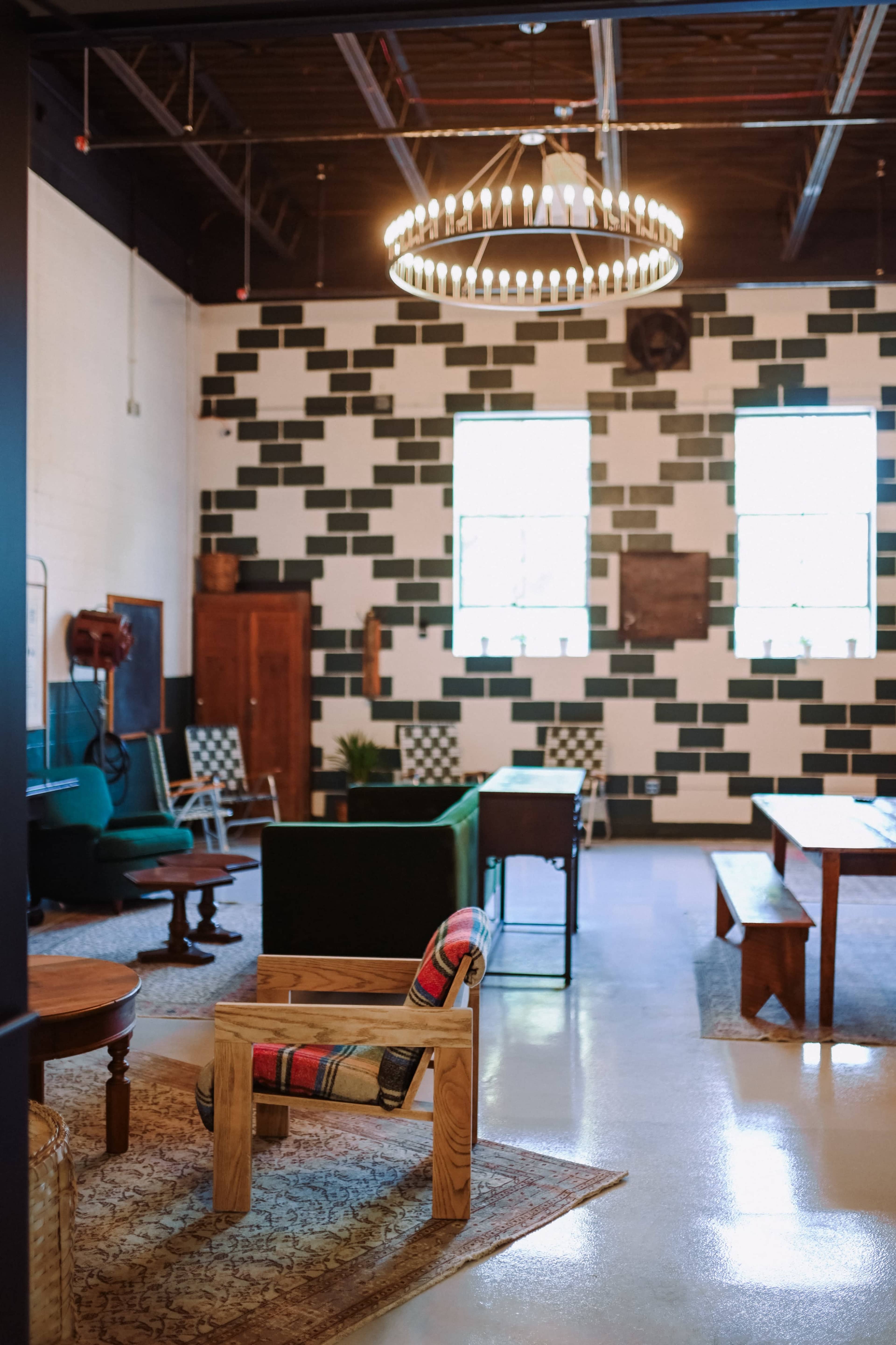 The image shows an interior space with a mix of wooden and upholstered furniture, featuring a round chandelier and walls accented by green and white paint.