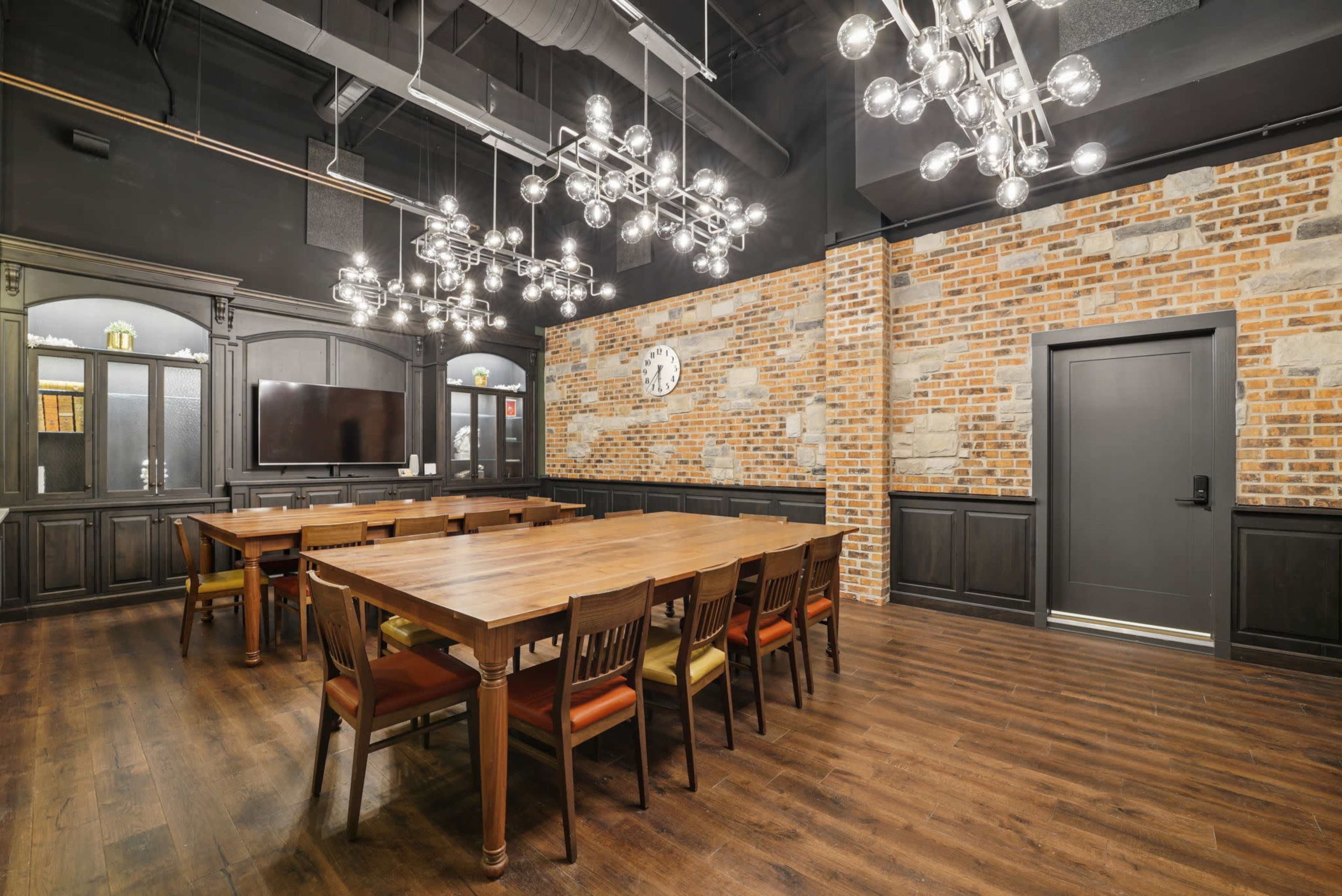 The image depicts a modern conference room with a large wooden table surrounded by chairs, complemented by industrial-style lighting and a brick wall.