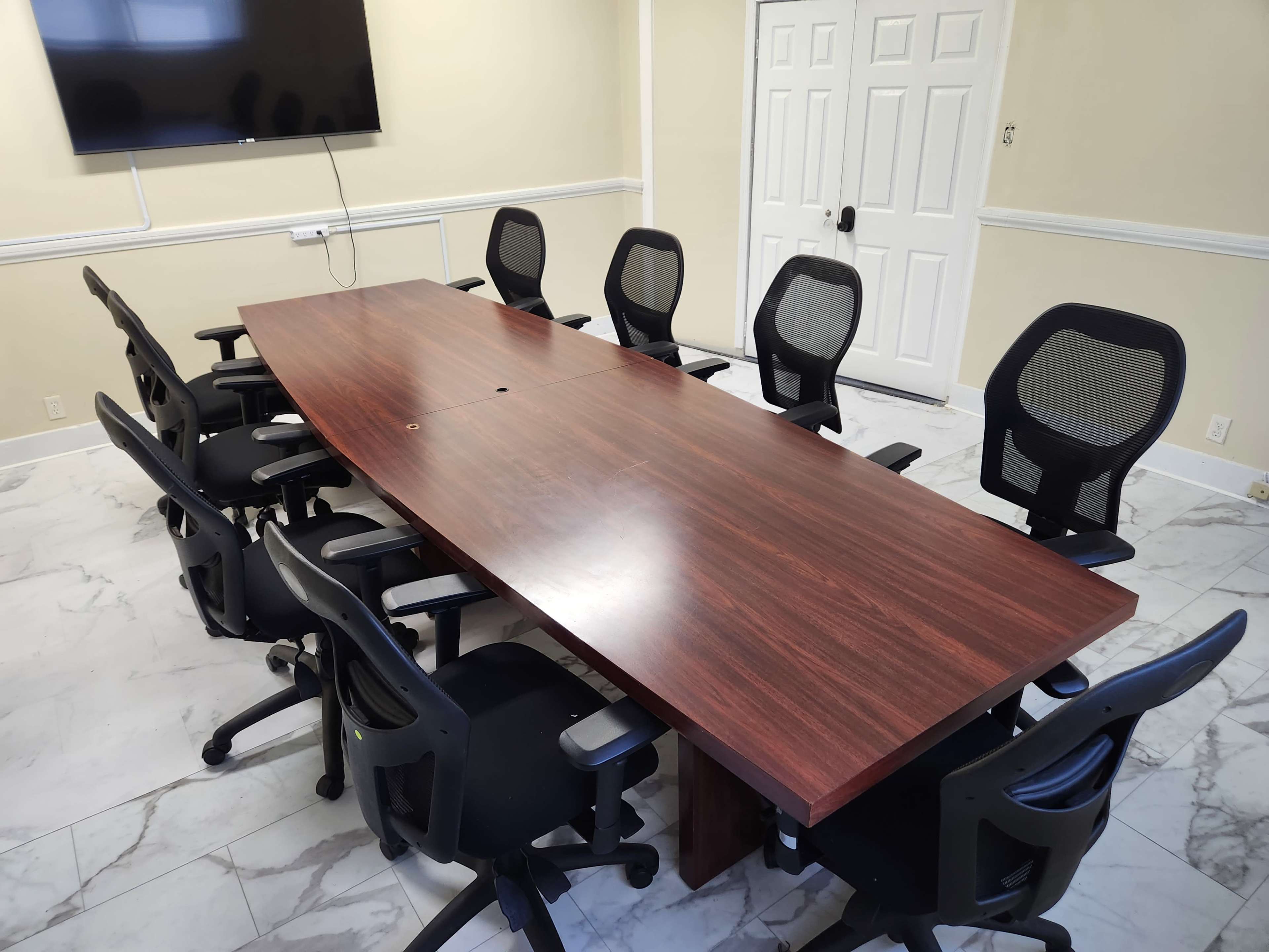 A large wooden conference table surrounded by multiple black ergonomic chairs in a meeting room.