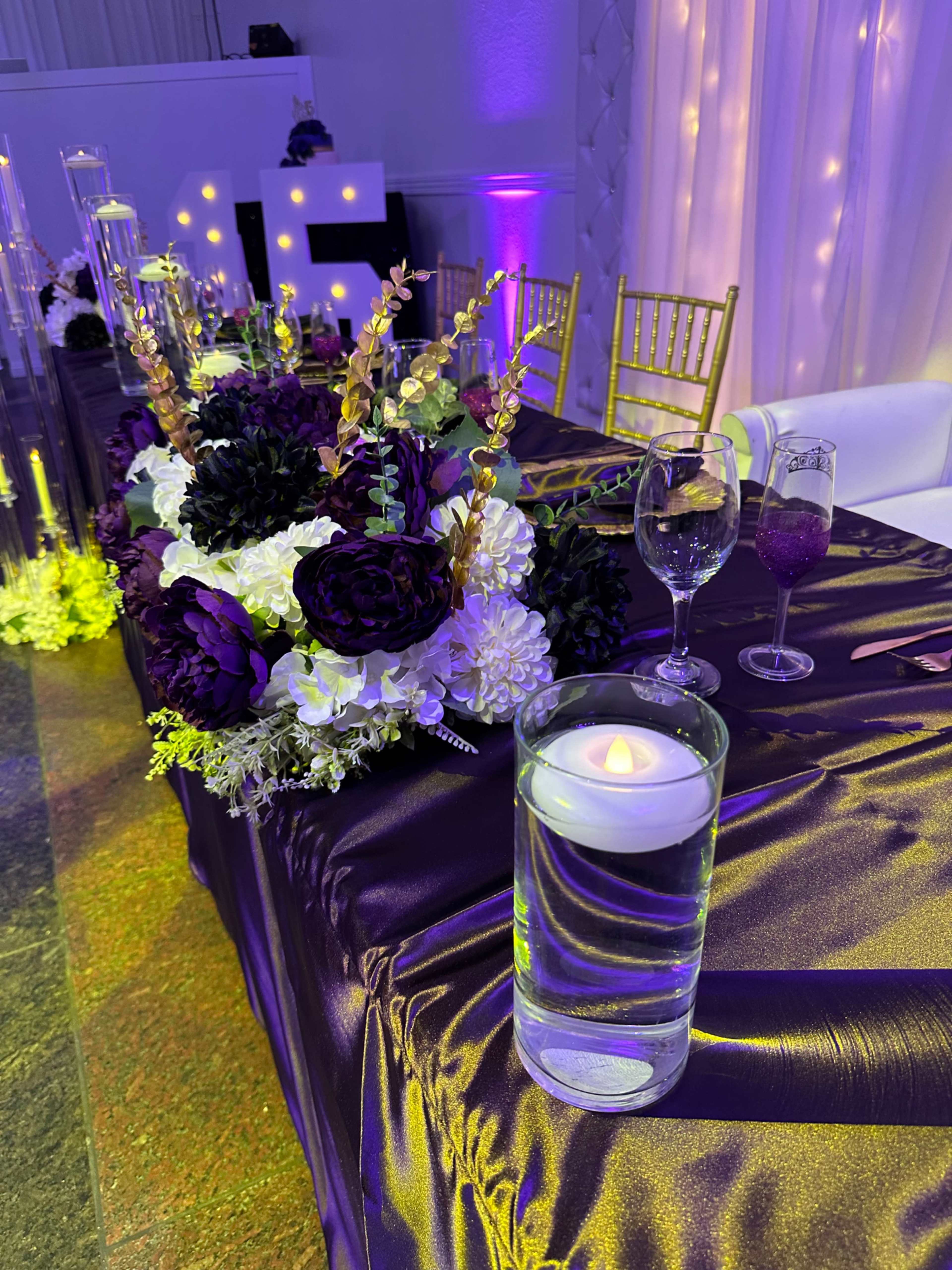 A floral arrangement featuring purple and white flowers decorates a table set with glassware and a floating candle.