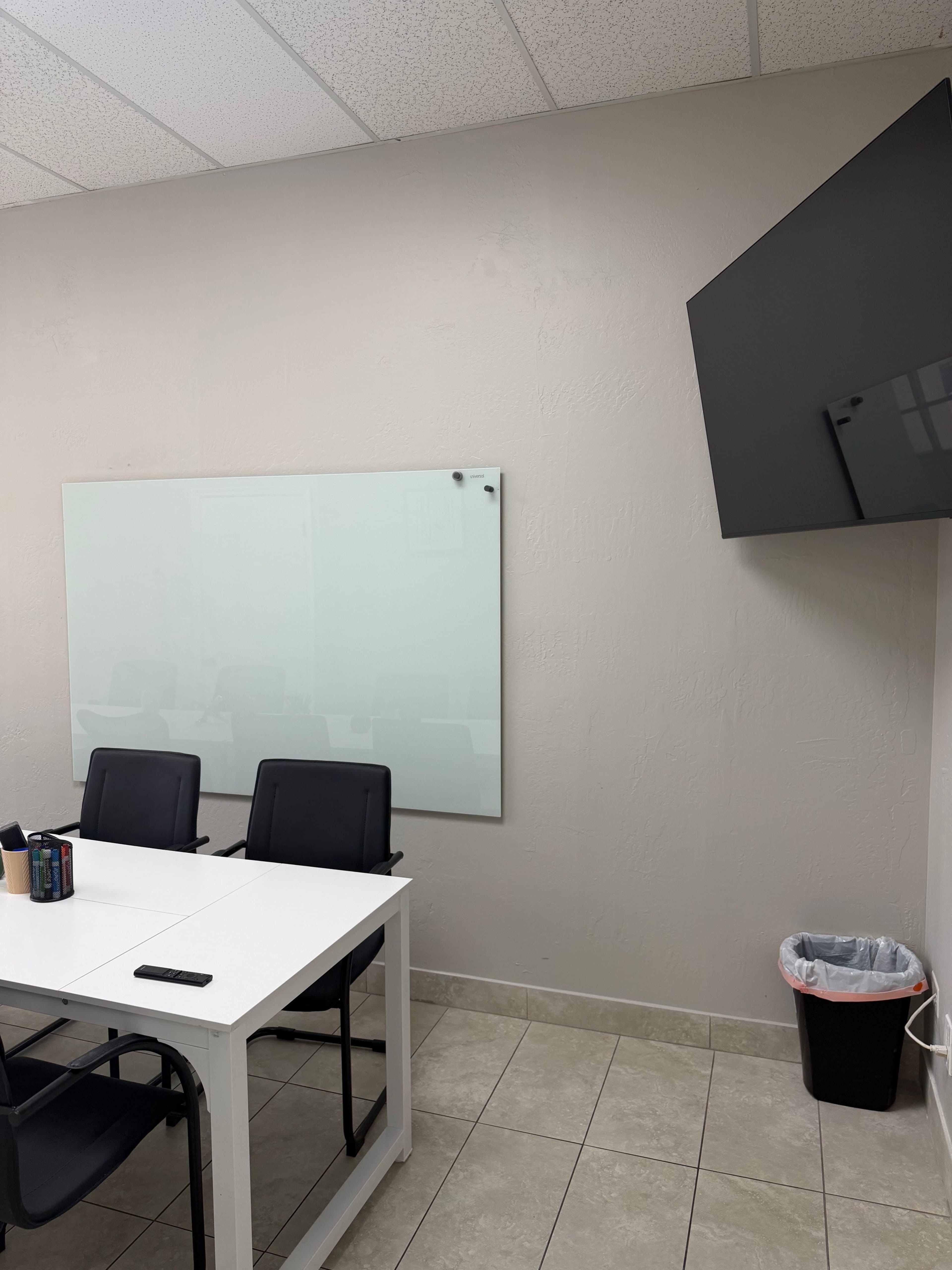 The image shows a conference room with a whiteboard, a television mounted on the wall, a table, and several chairs arranged around it.