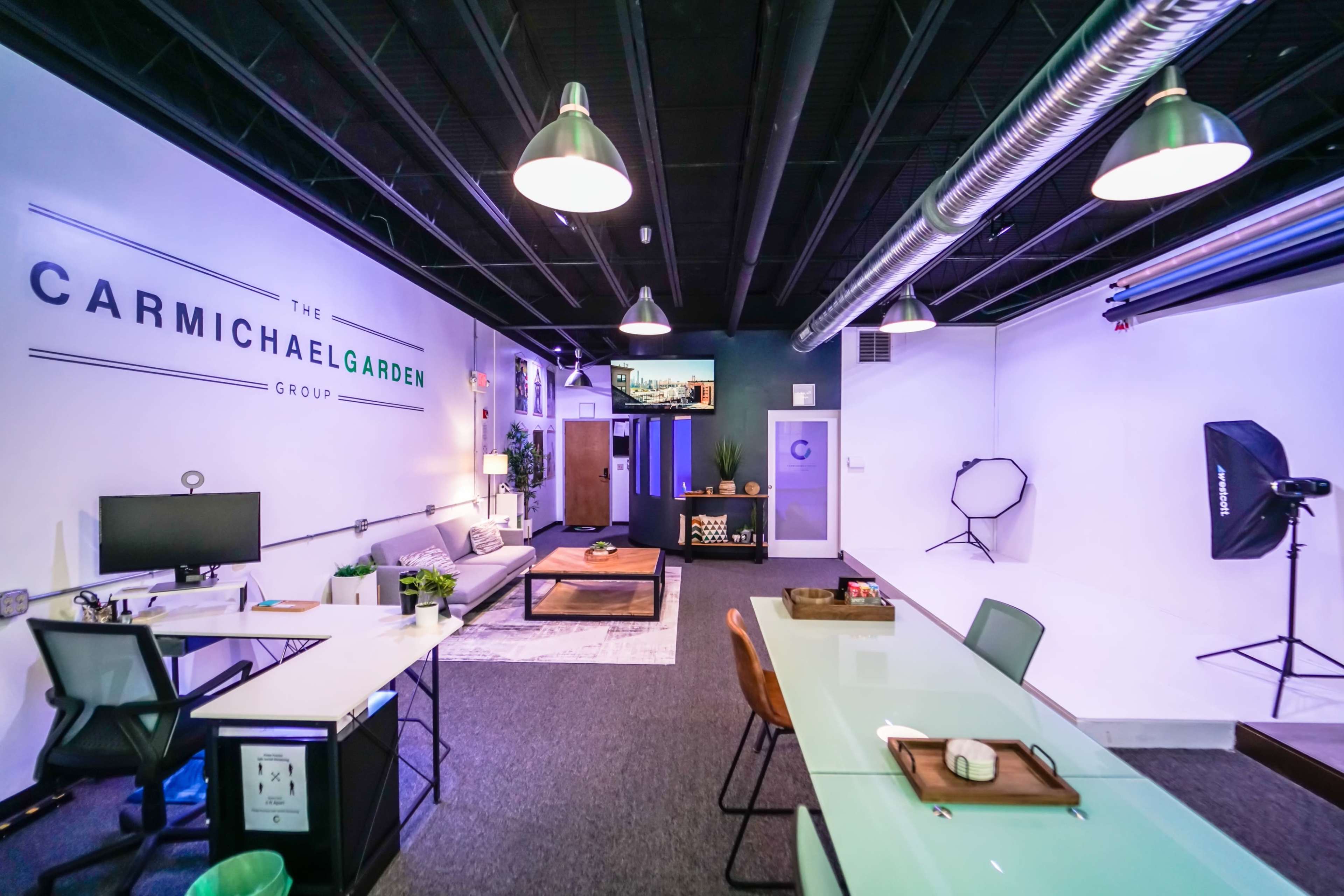 A modern office space featuring desks, a lounge area, and branding for "The Carmichael Garden Group" on the wall.