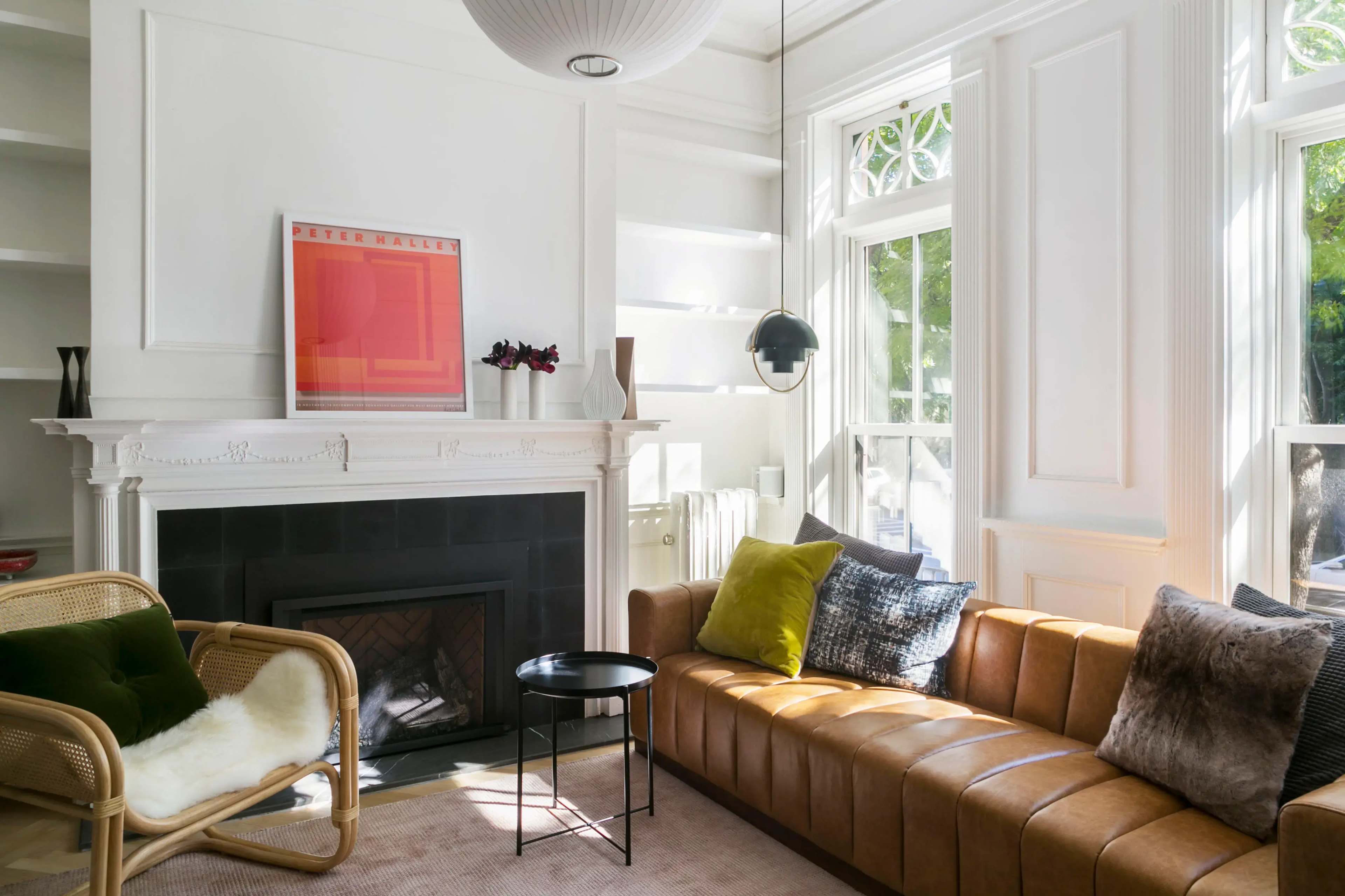 A modern living room with a brown leather sofa, a round black coffee table, a fireplace, and large windows allowing natural light to enter the space.