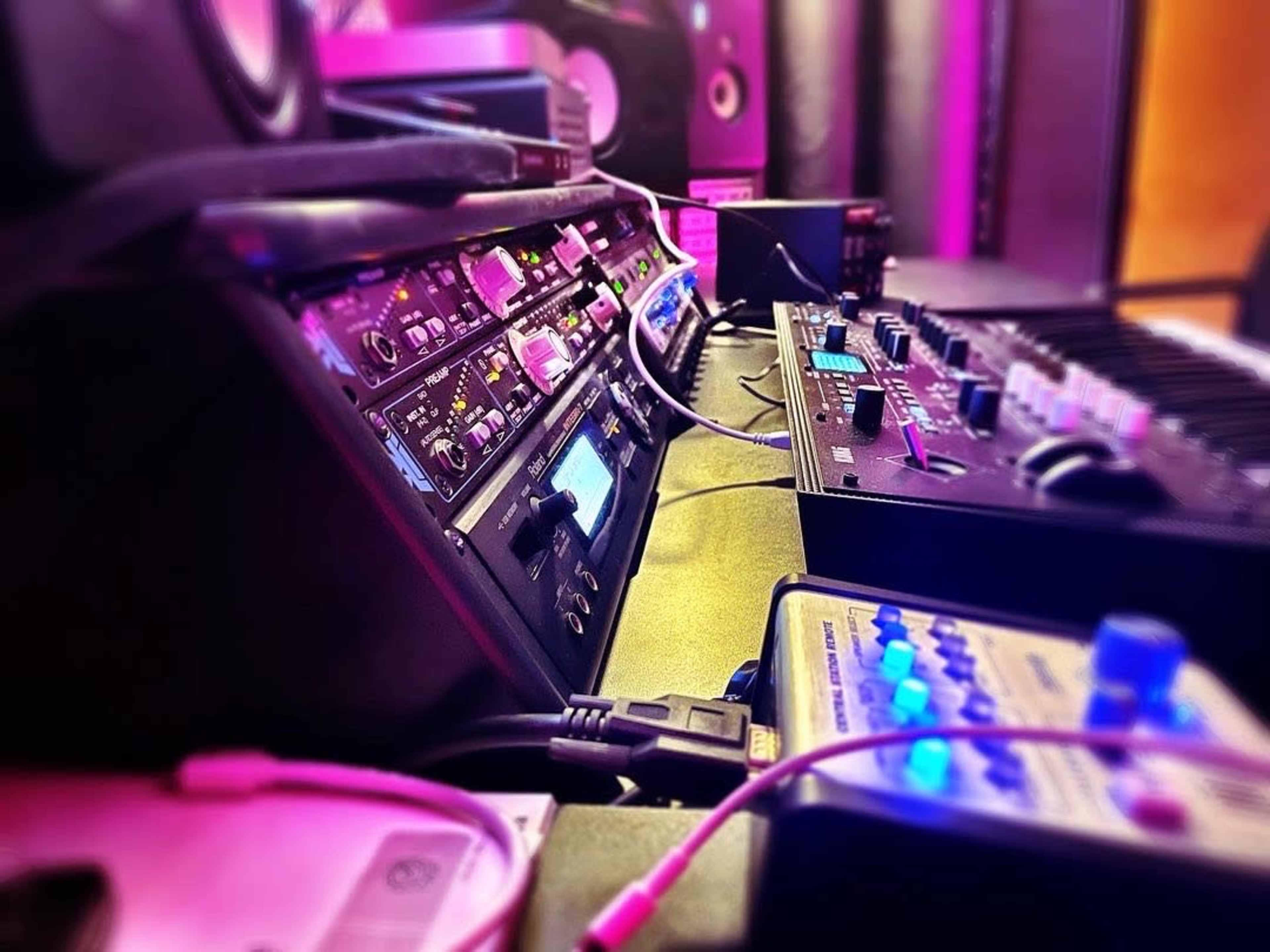 The image shows a close-up view of audio equipment and synthesizers in a music studio setting.