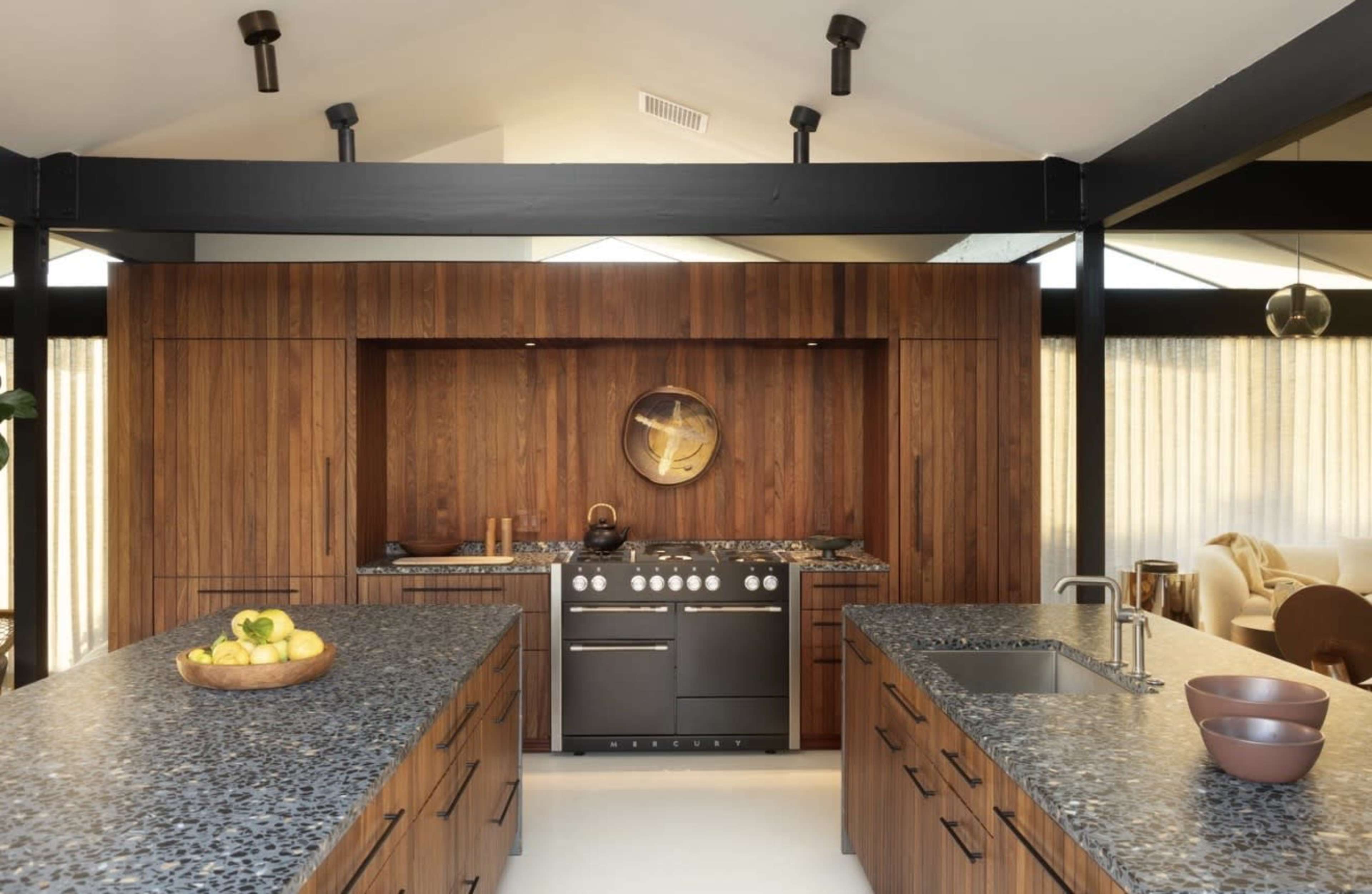 The image shows a modern kitchen featuring dark wood cabinetry, a central island with a stone countertop, and stainless steel appliances.
