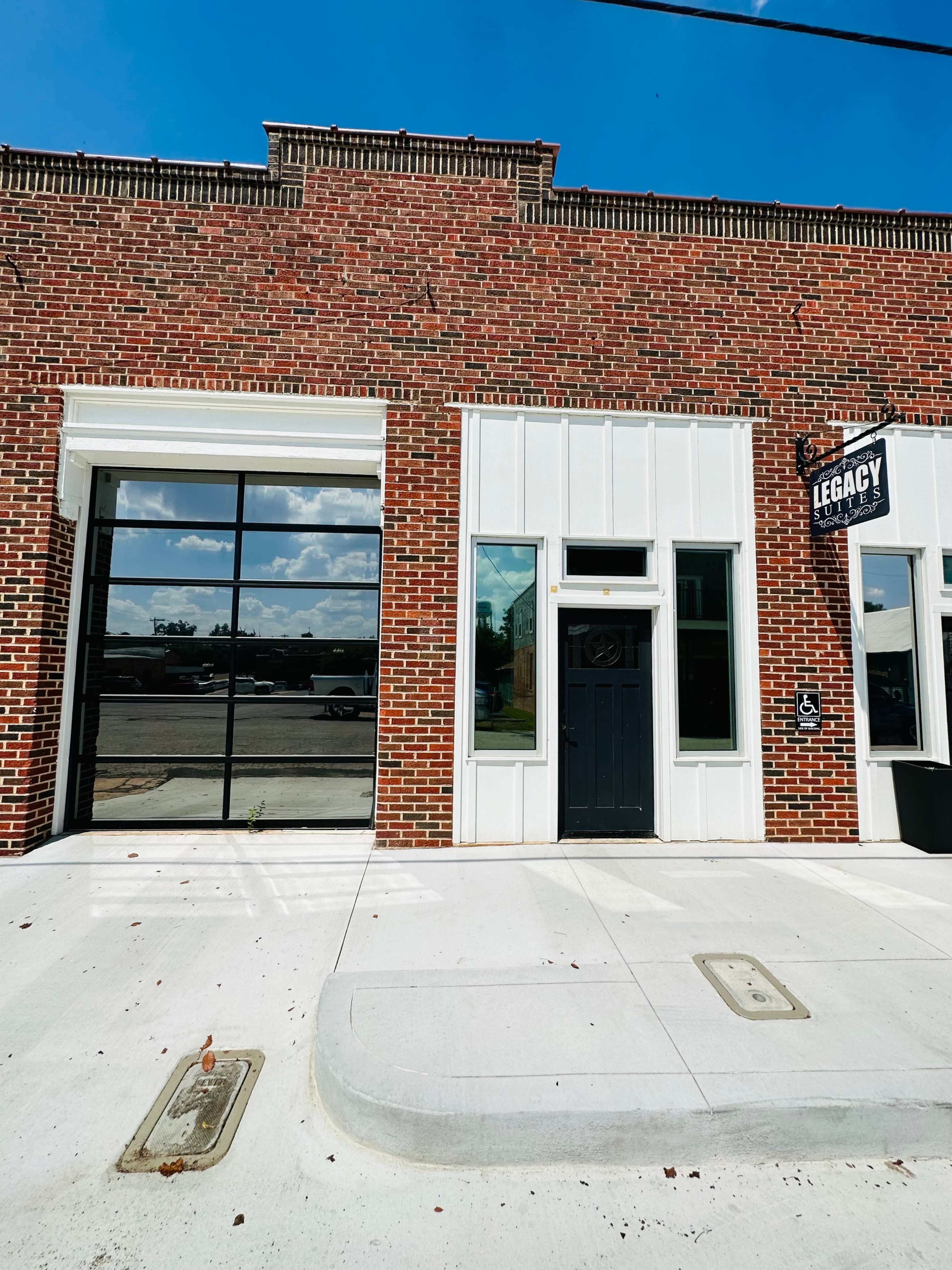 A red brick building with a large glass window and a black door, featuring a sign that reads "Legacy."
