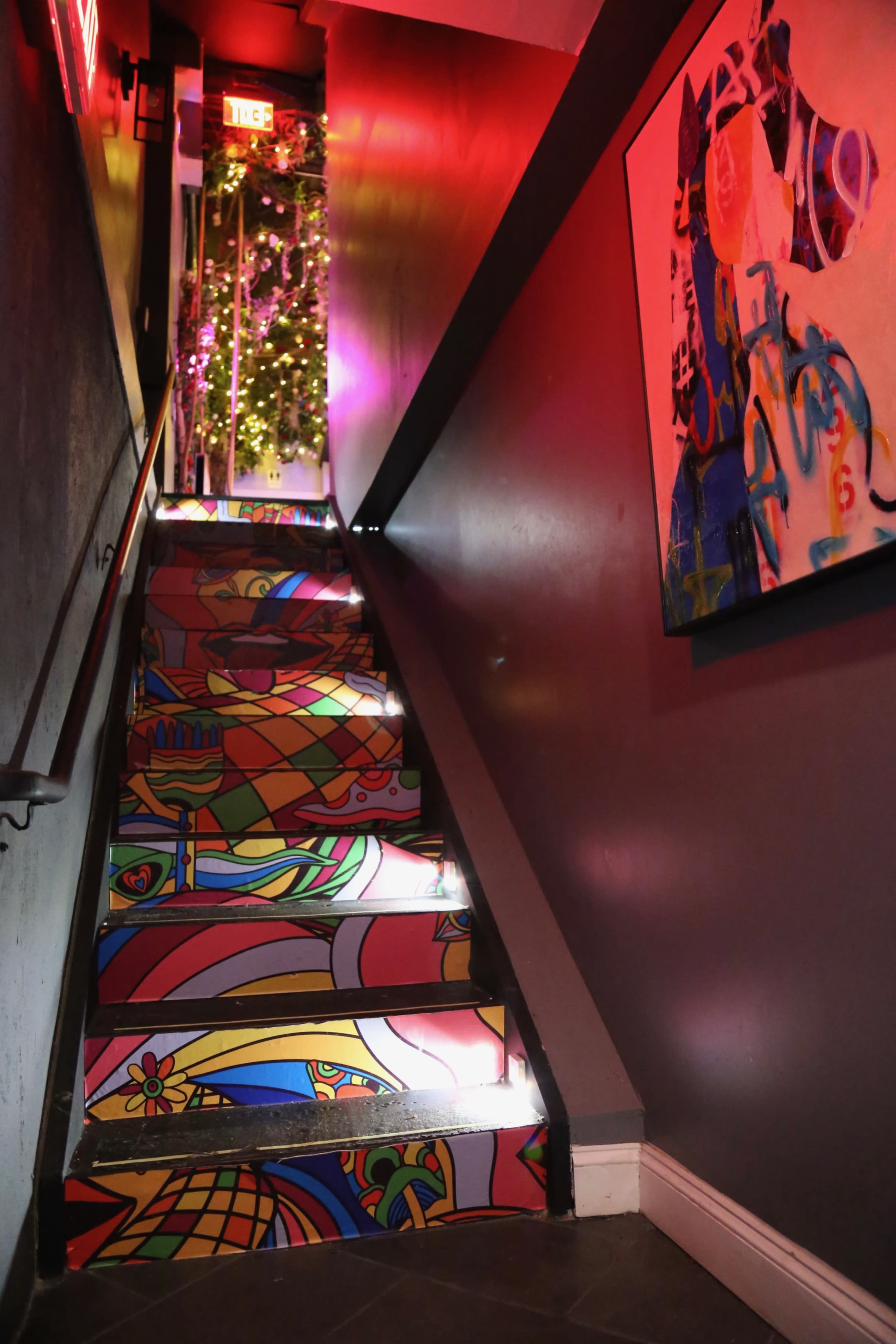 A brightly colored staircase leads up to a door illuminated by red exit signs, with a decorated tree visible at the top.