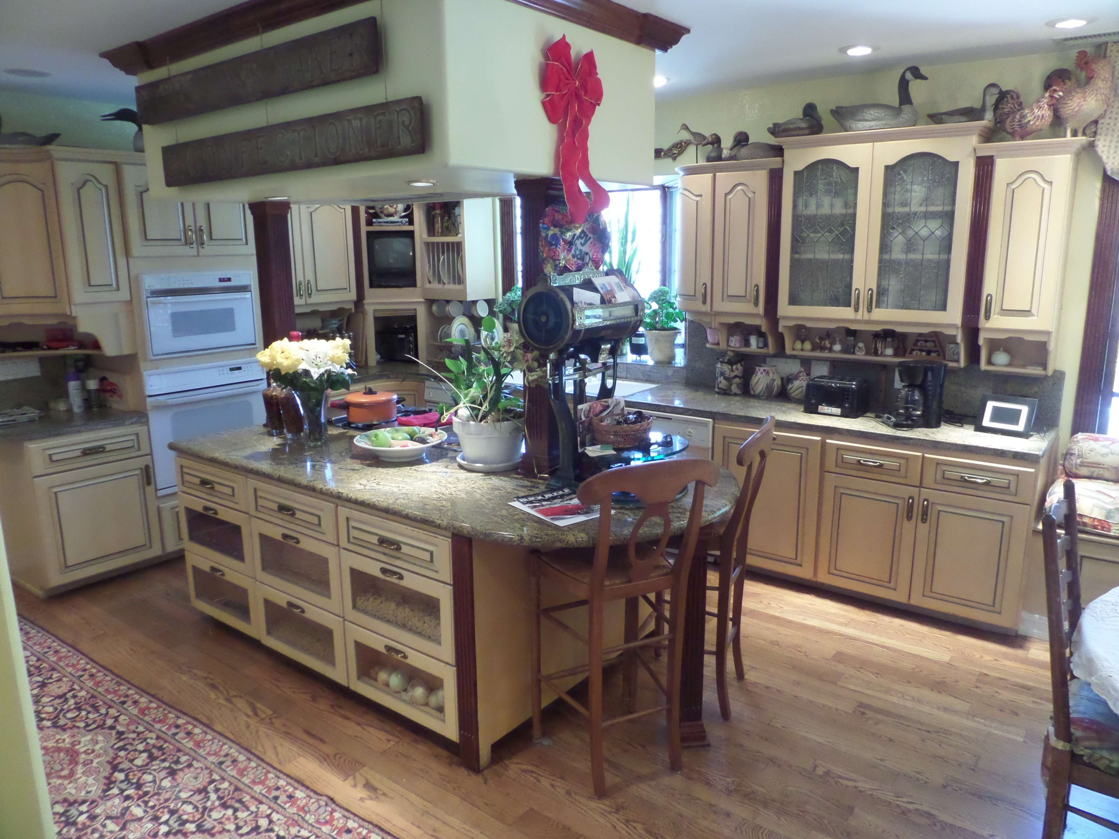 A warm, inviting kitchen with wooden cabinetry, a central island, and various kitchen appliances, adorned with decorative items and fresh flowers on the counter.