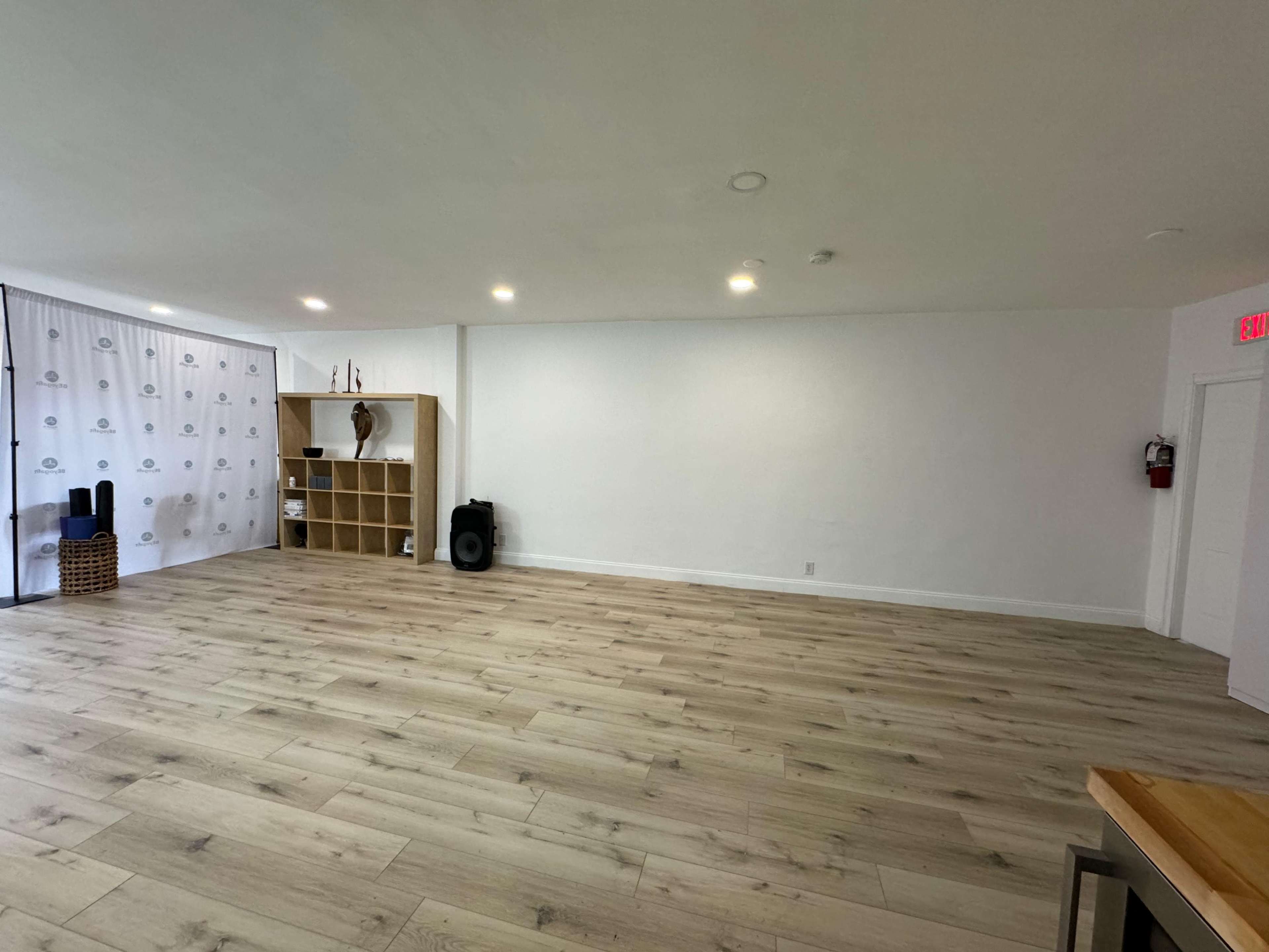 A spacious room with light wooden flooring, a simple bookshelf, and a backdrop featuring a patterned curtain.