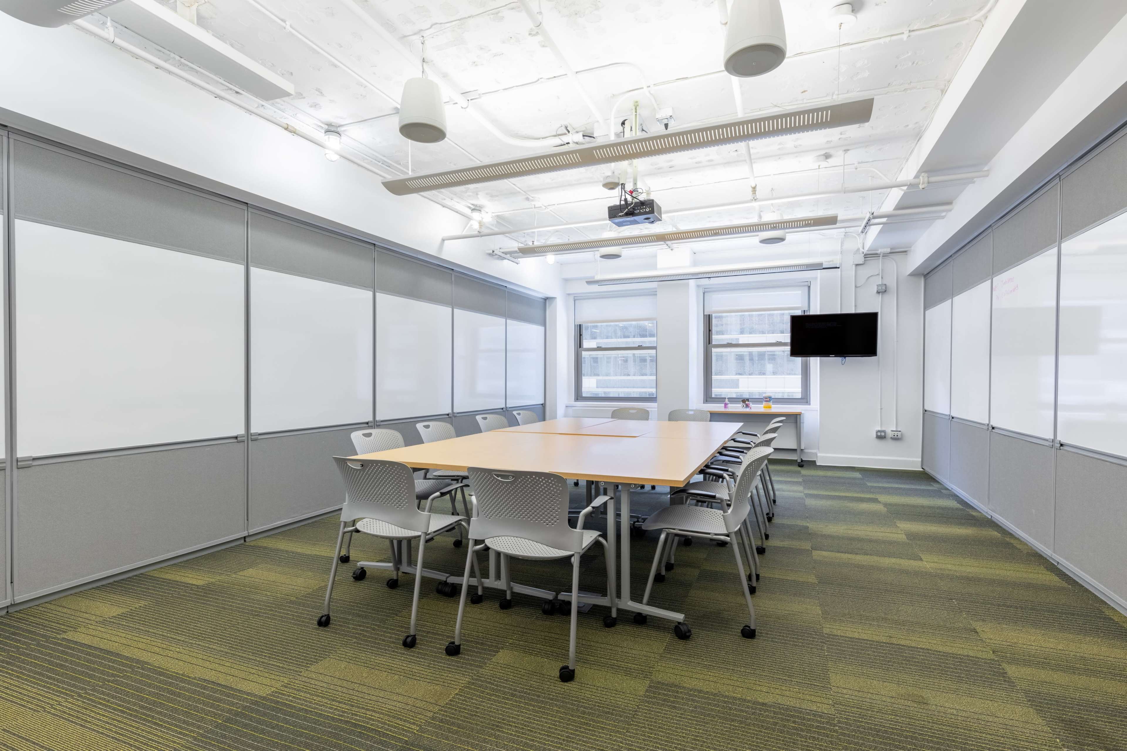 A conference room with a large table surrounded by chairs, whiteboards on the walls, and a projector and screen at one end.