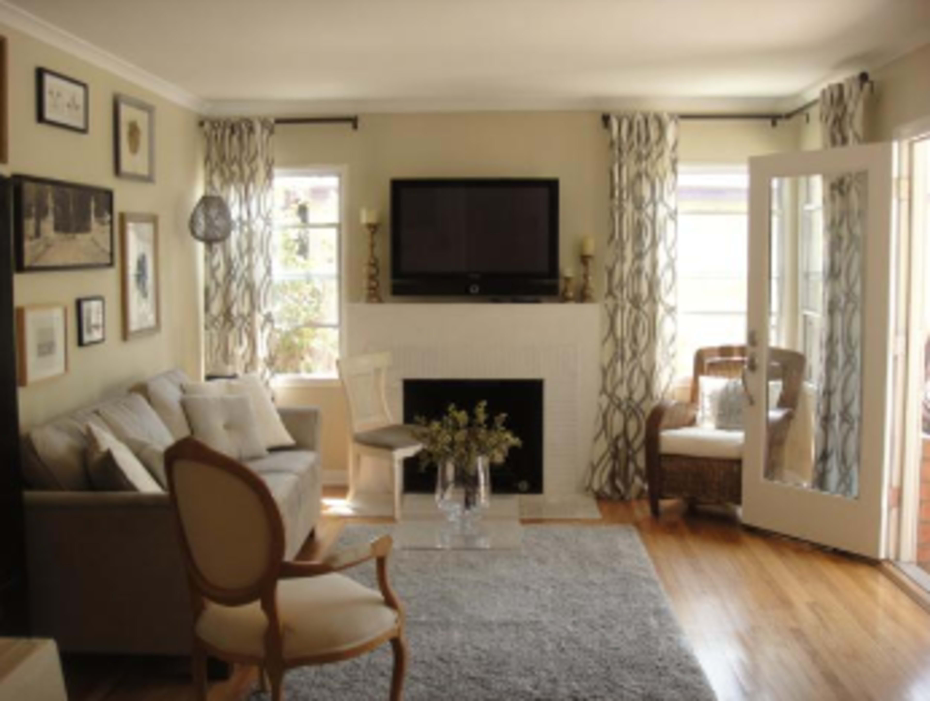 The living room features a sofa, a television mounted above a white fireplace, and large windows with light curtains.