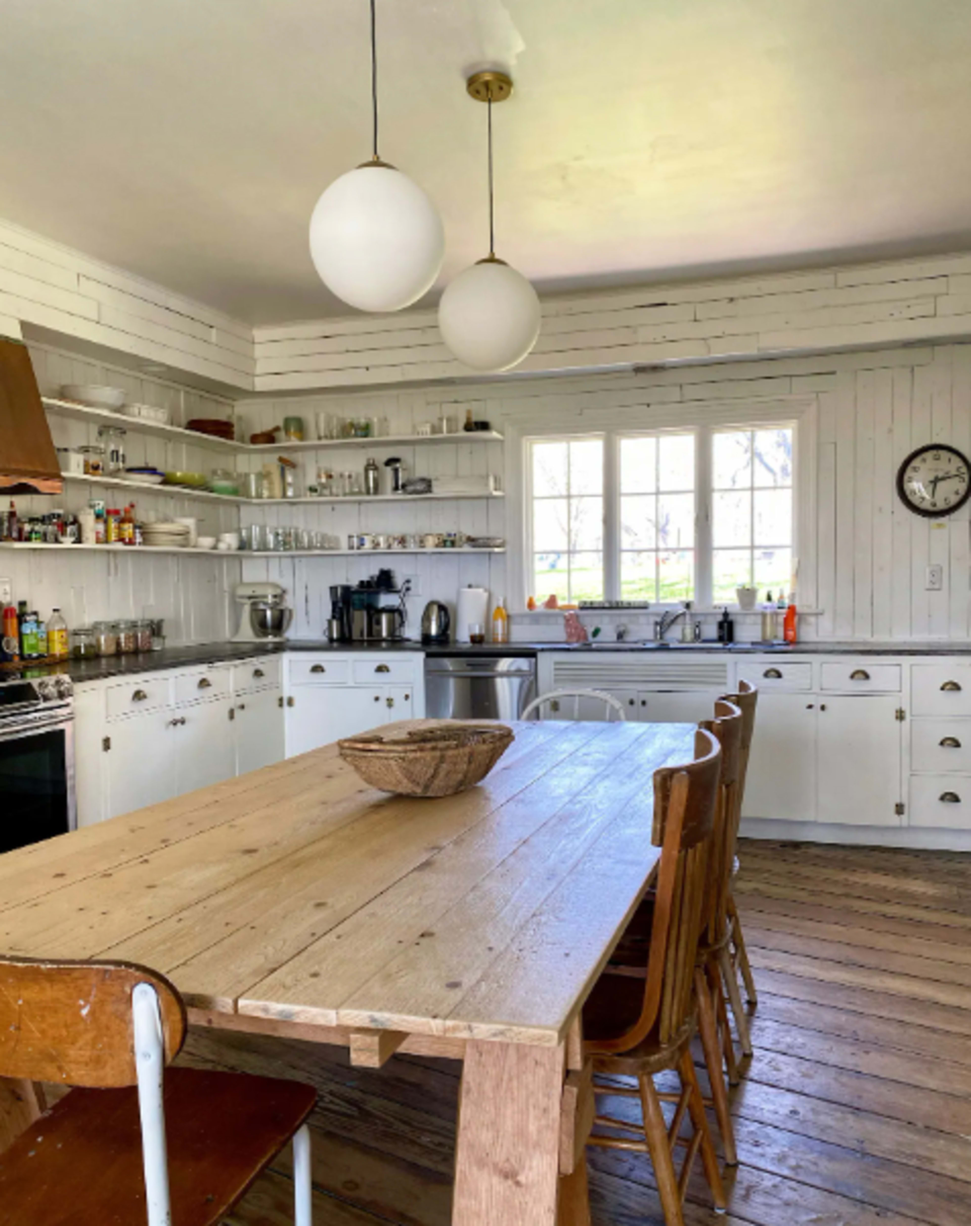 A spacious kitchen features white cabinetry and shelves filled with jars and utensils, along with a wooden table and six chairs.
