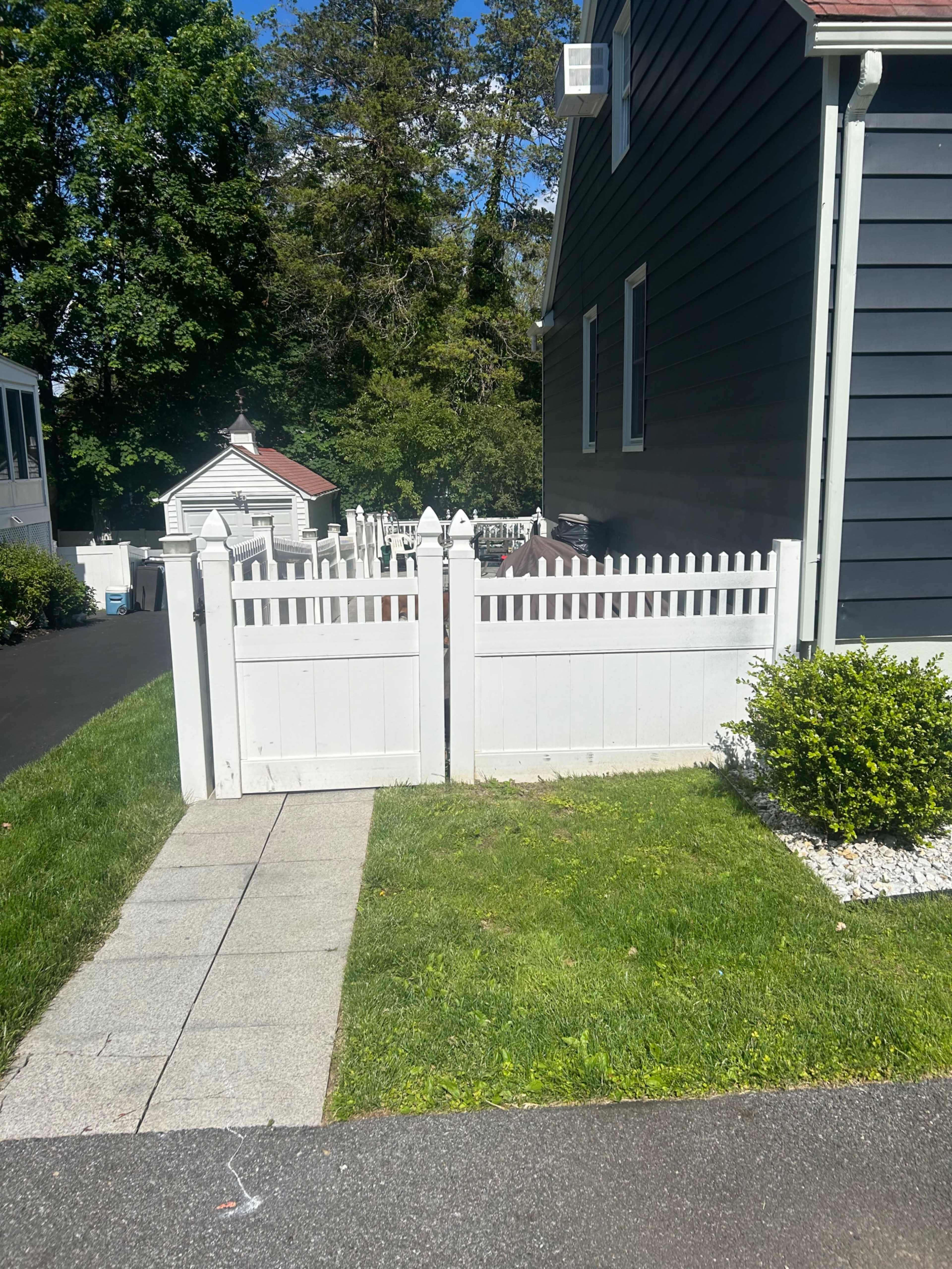 A white picket fence encloses a small area behind a house, with a stone walkway leading to it.