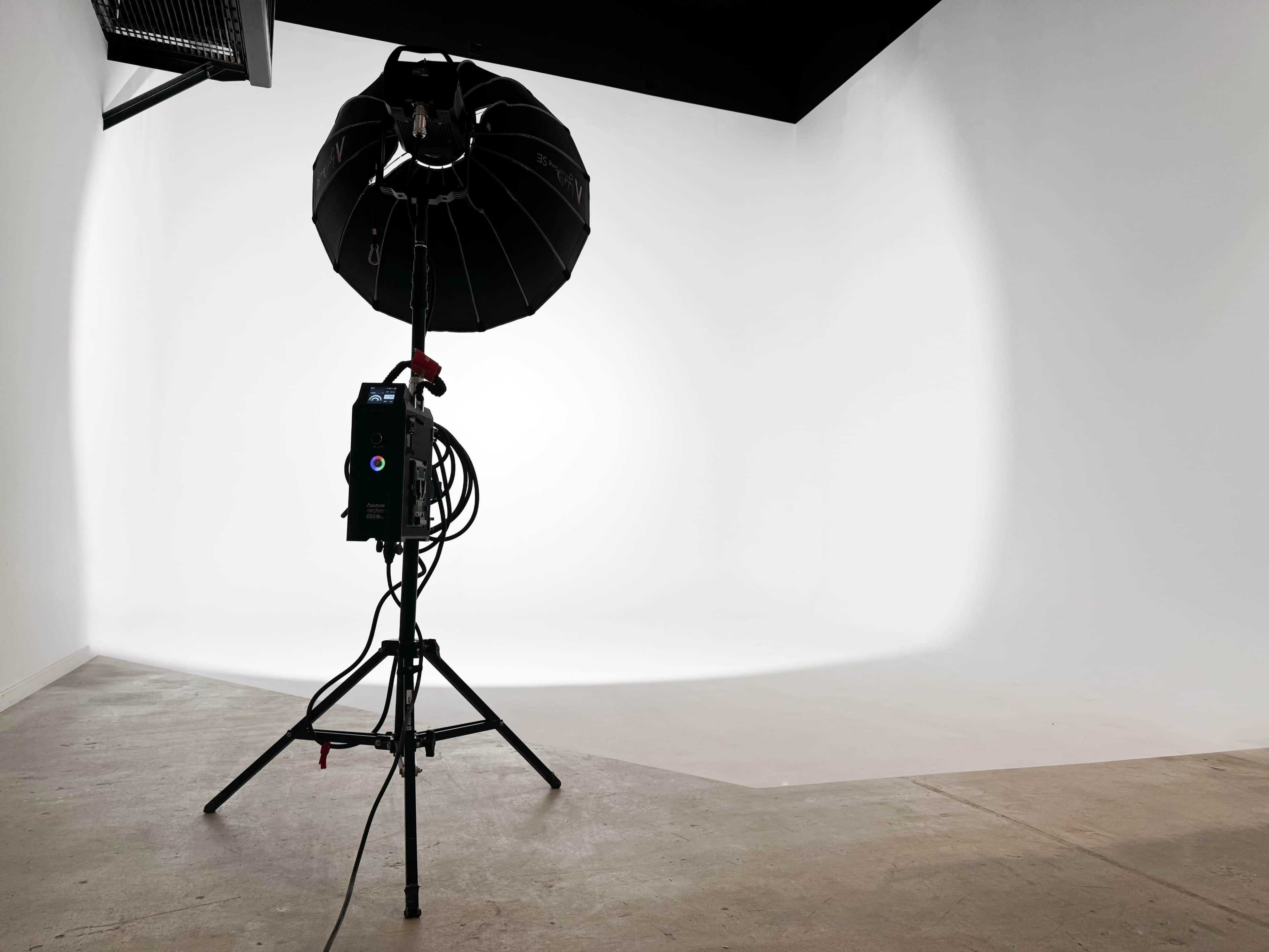 A professional studio lighting setup stands on a concrete floor in a minimalist white backdrop space.