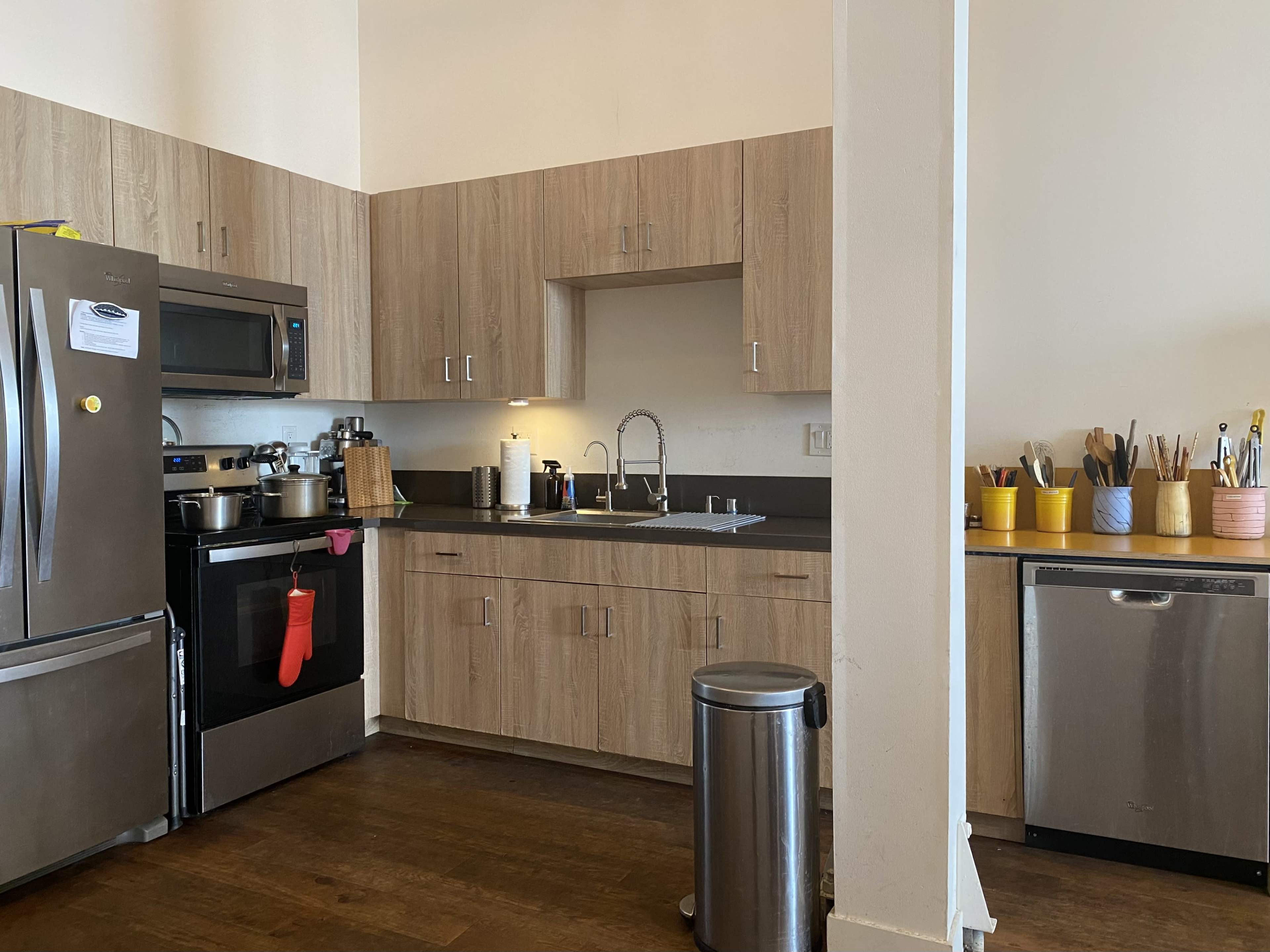 A modern kitchen with wooden cabinets, stainless steel appliances, a sink, and colorful utensil holders on the countertop.
