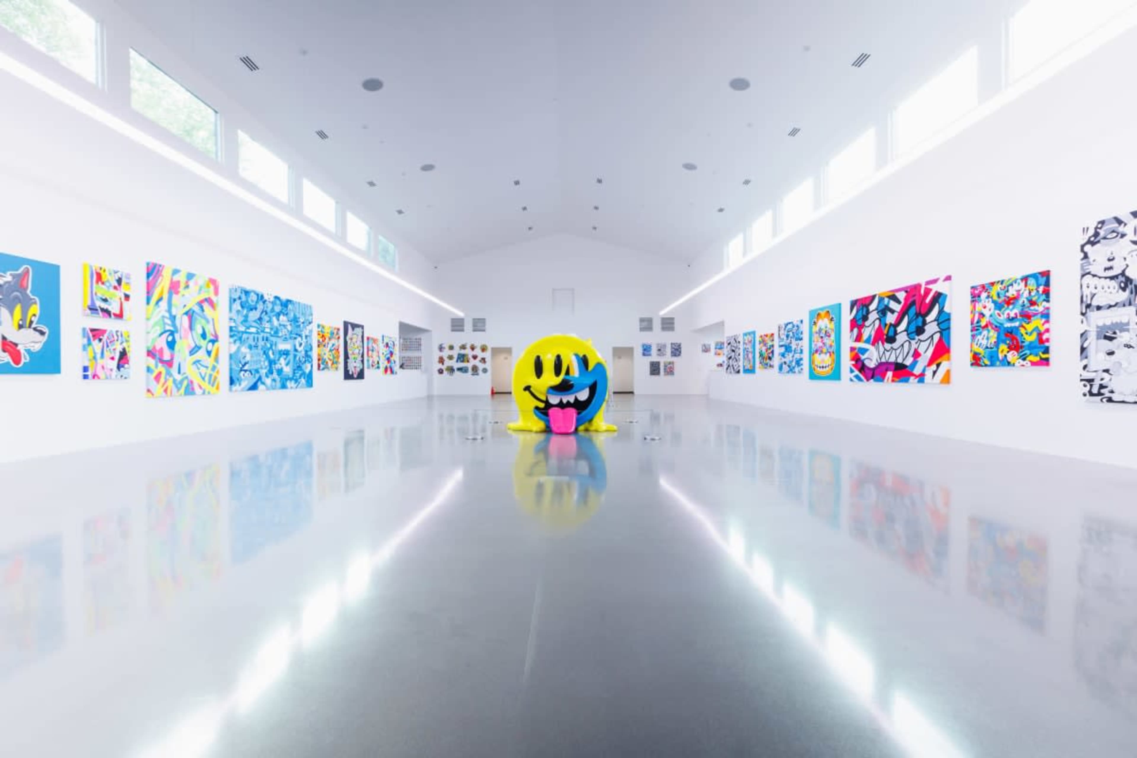 The interior of a modern art gallery features colorful artworks on the walls and a large, cartoonish sculpture in the center.