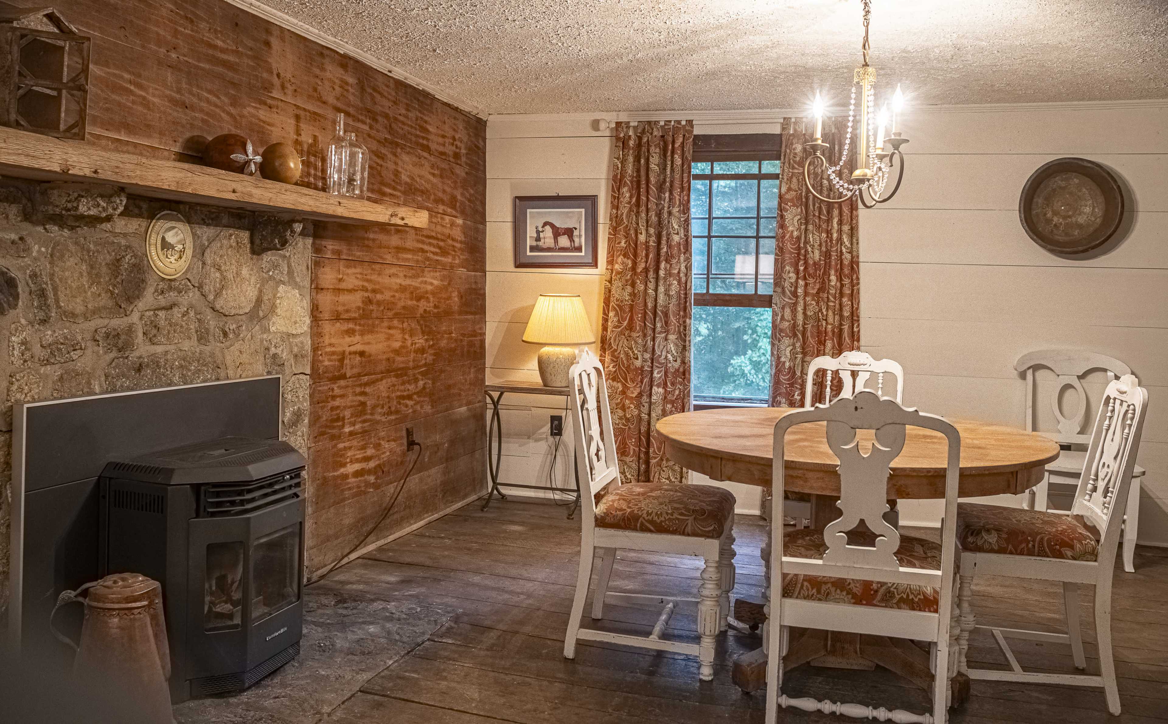 A cozy dining area featuring a round wooden table surrounded by four white chairs, a stone fireplace, and a light fixture hanging overhead.
