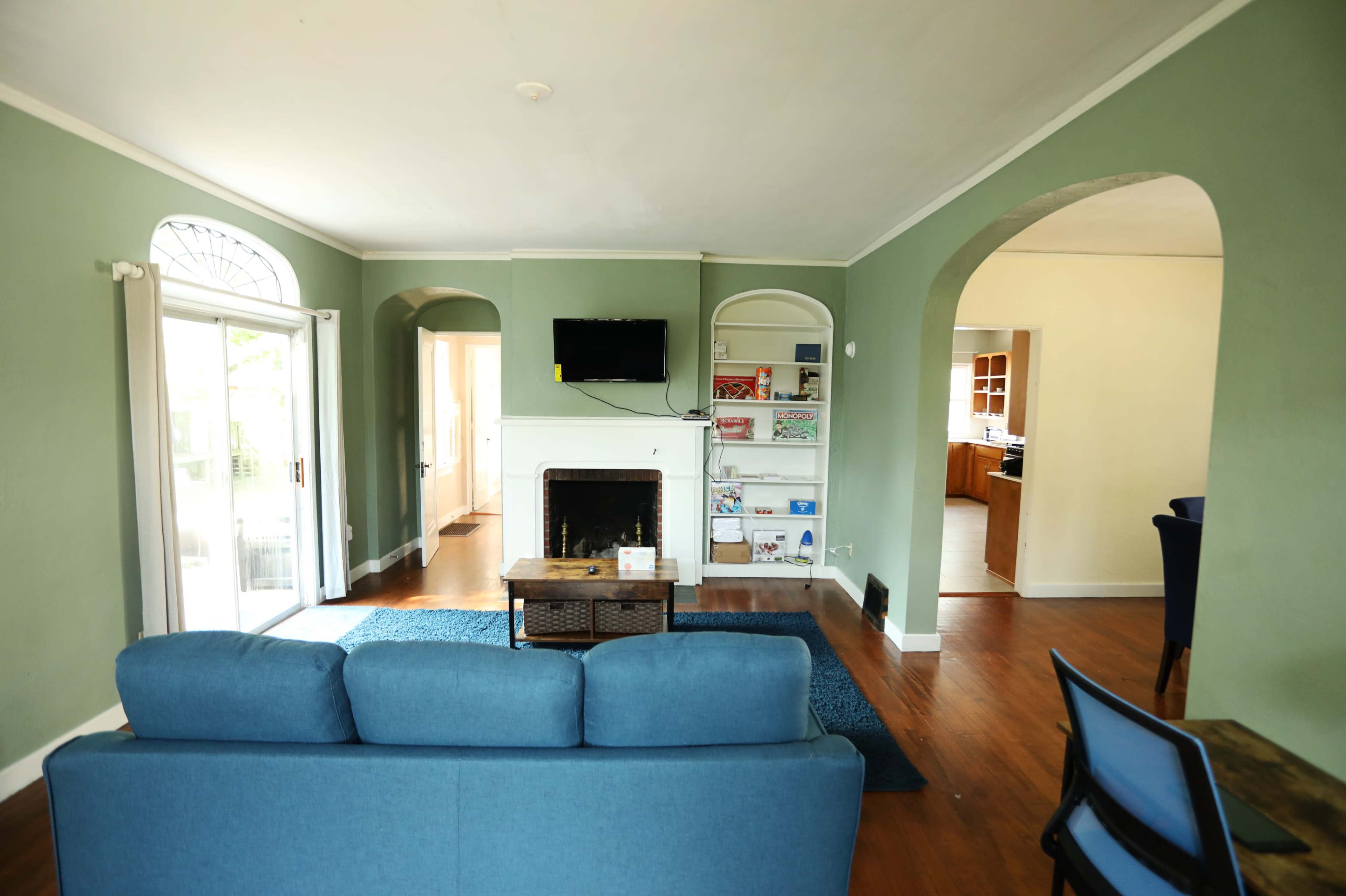 The image shows a living room with green walls, a blue sofa, a fireplace, and arched doorways leading to a kitchen area.