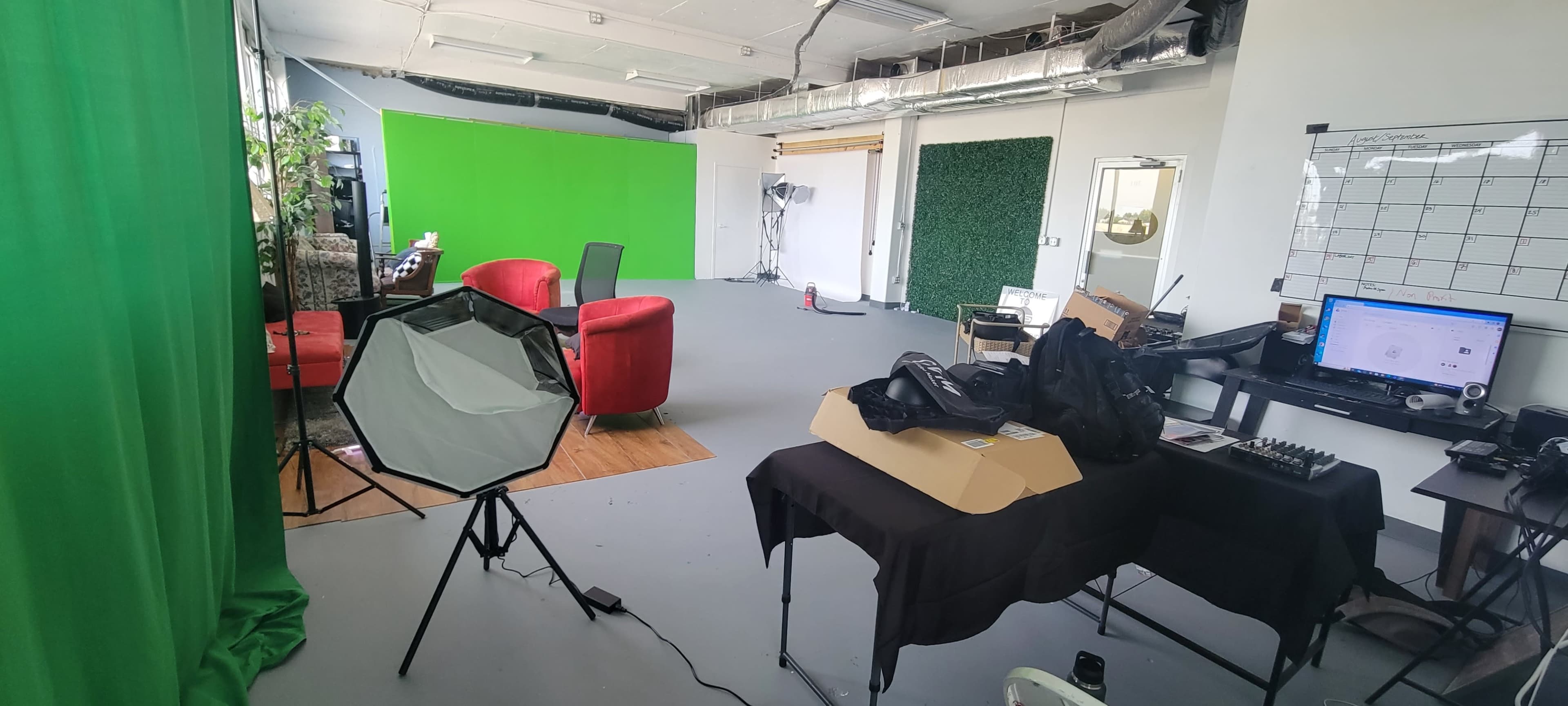 A studio space featuring green screens, red chairs, a light setup, and various equipment on tables.