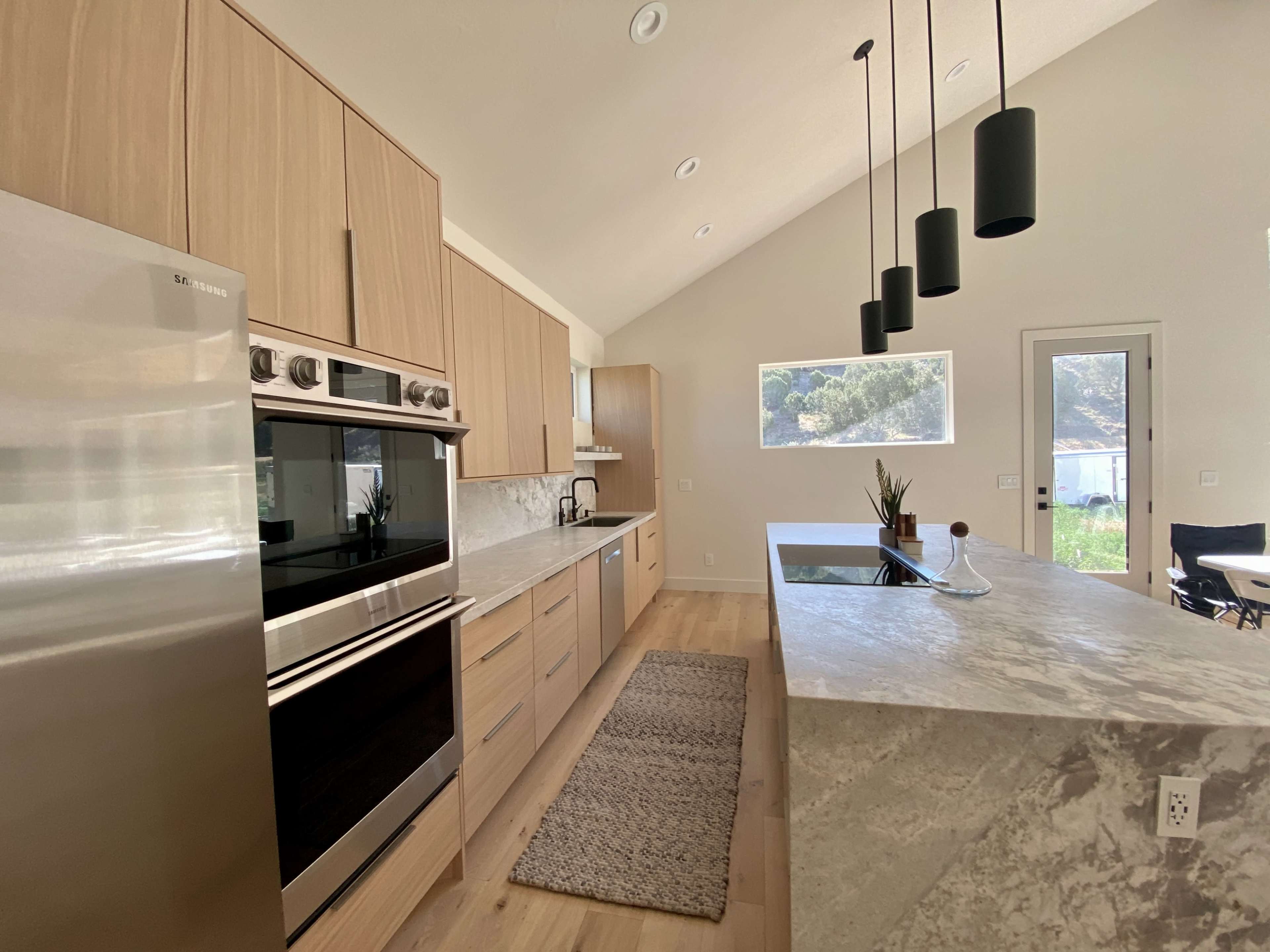 The image shows a modern kitchen with light wood cabinetry, stainless steel appliances, and a marble-topped island.