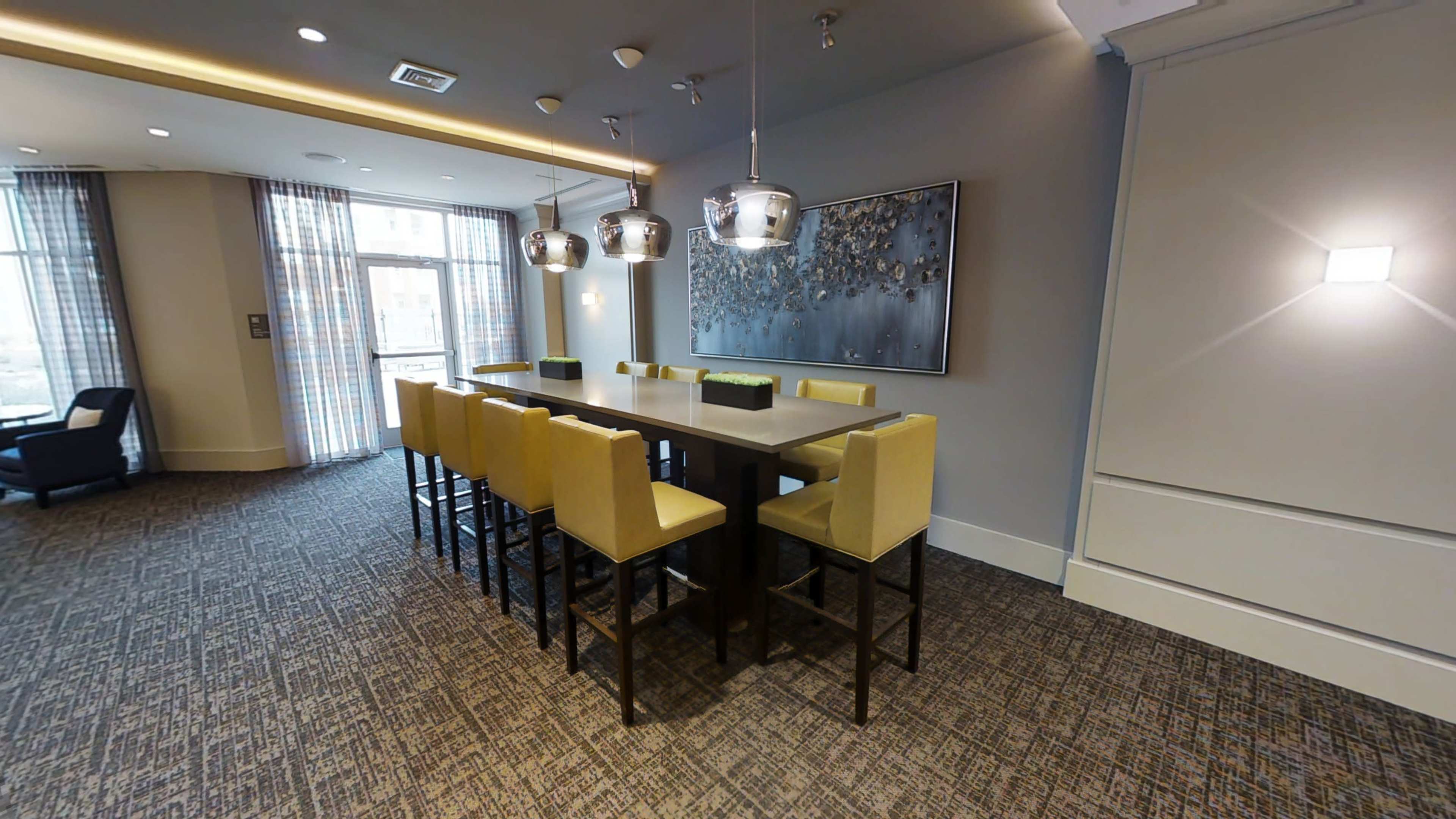 A modern dining area with a long table and yellow upholstered chairs, illuminated by stylish pendant lights.