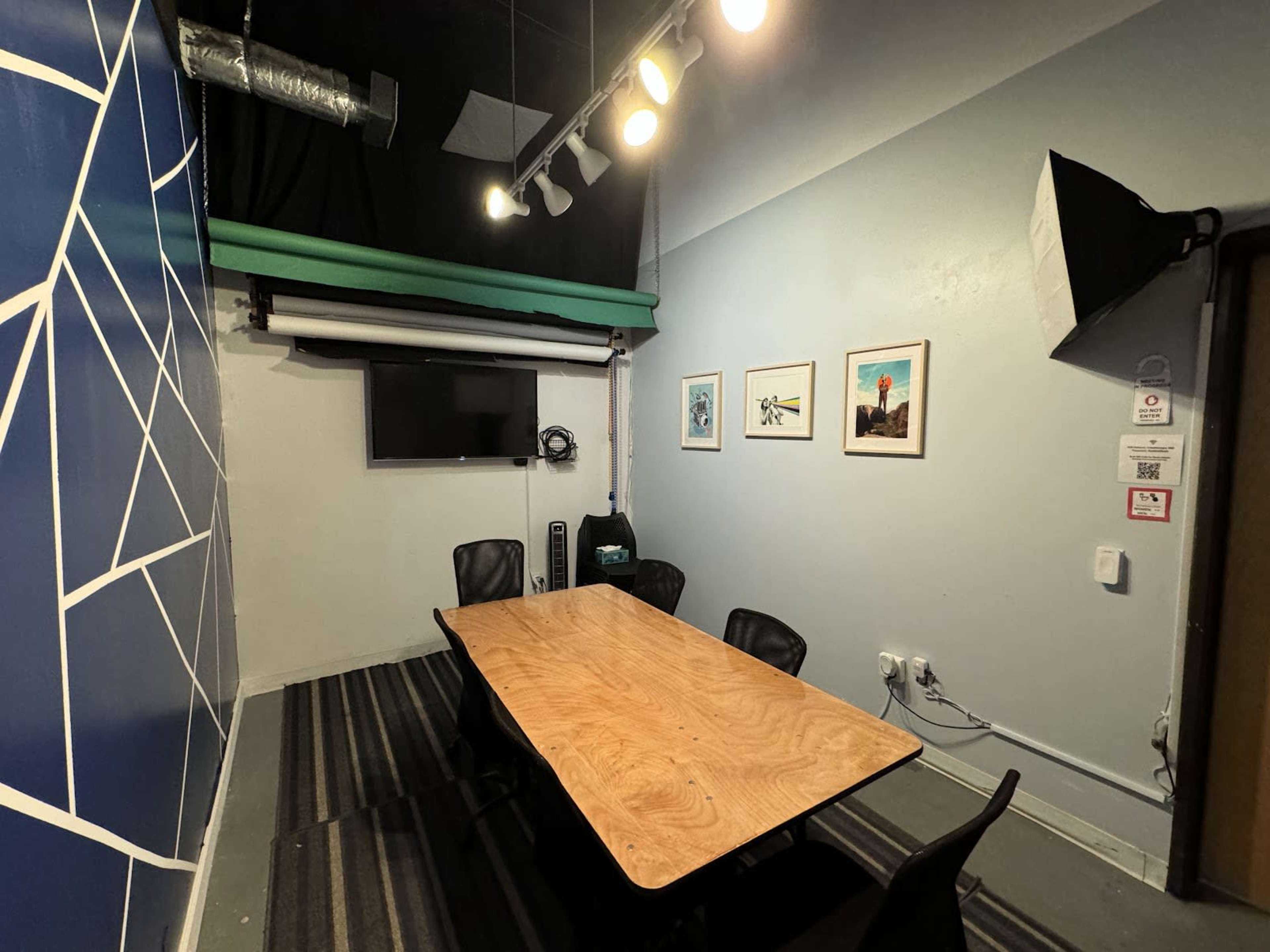 A small conference room with a wooden table, black chairs, a wall-mounted TV, and artwork displayed on the walls.