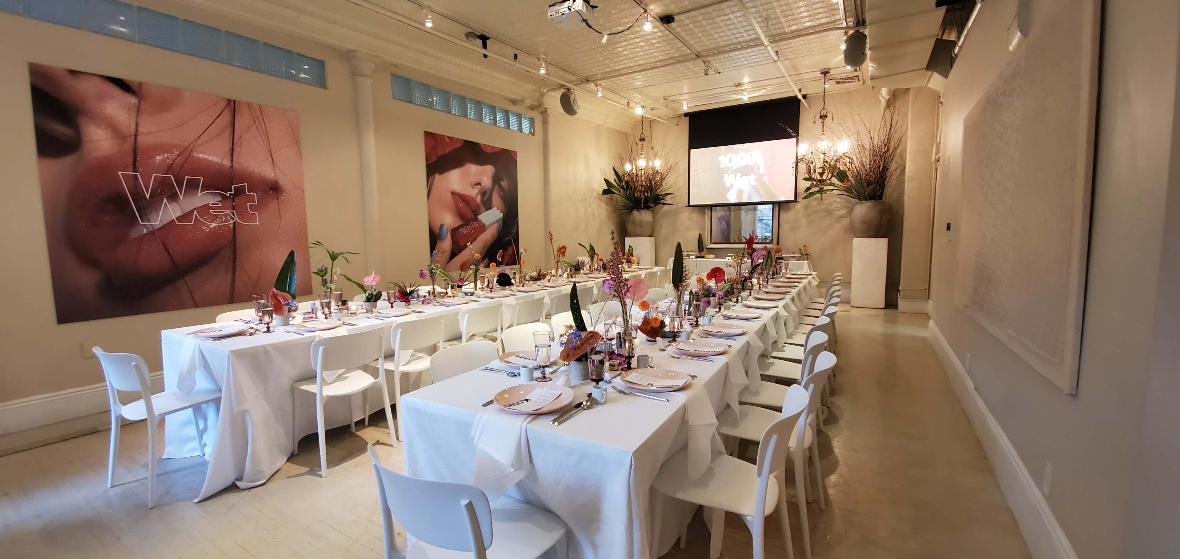 A long, elegantly set dining table is arranged in a brightly lit room adorned with modern artwork and floral decorations.