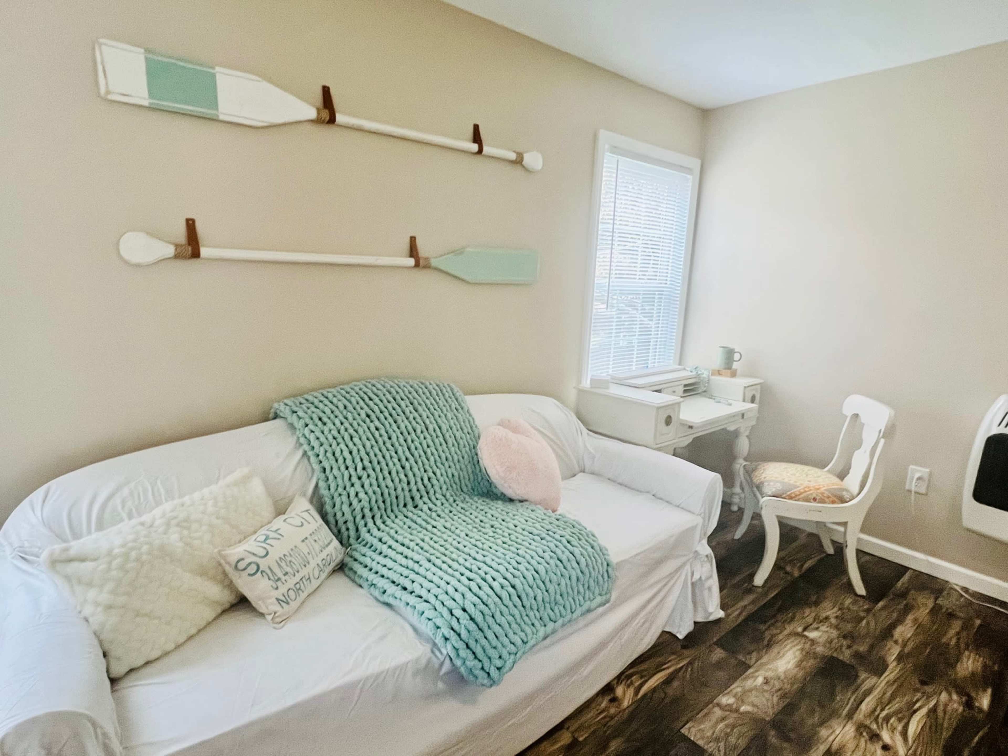 A cozy room featuring a white couch with a blue blanket, decorative pillows, and a small desk next to a chair.