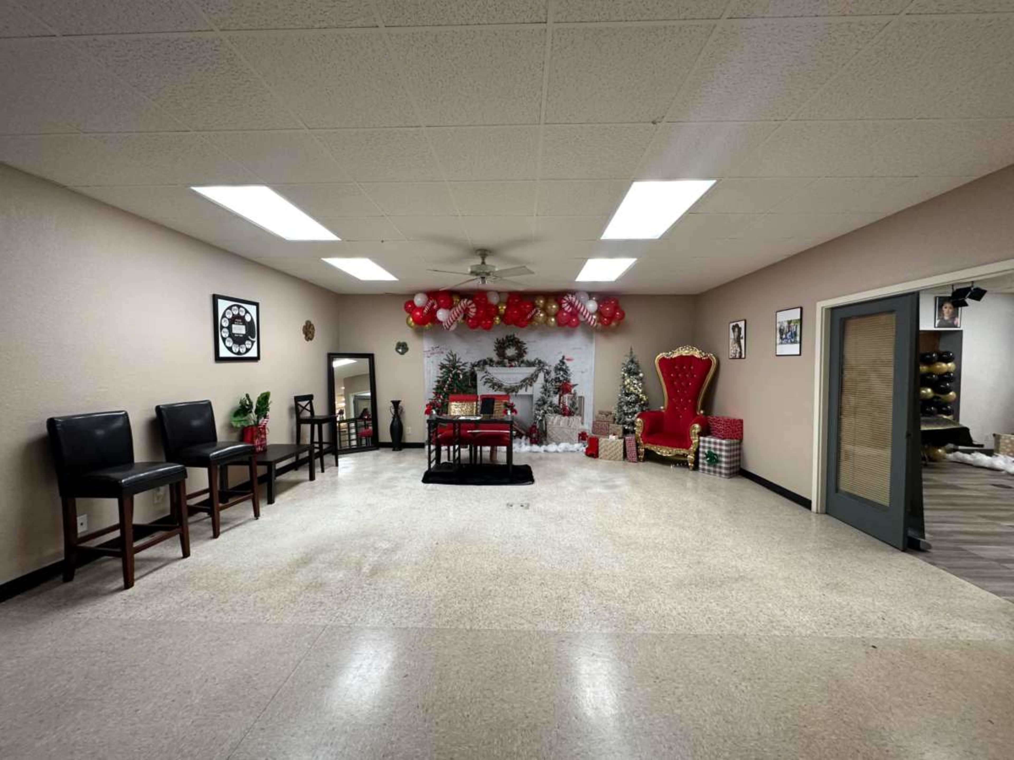 The image shows a spacious room decorated with festive balloons, a Christmas tree, and a large red throne-like chair, along with several black chairs arranged along one side.