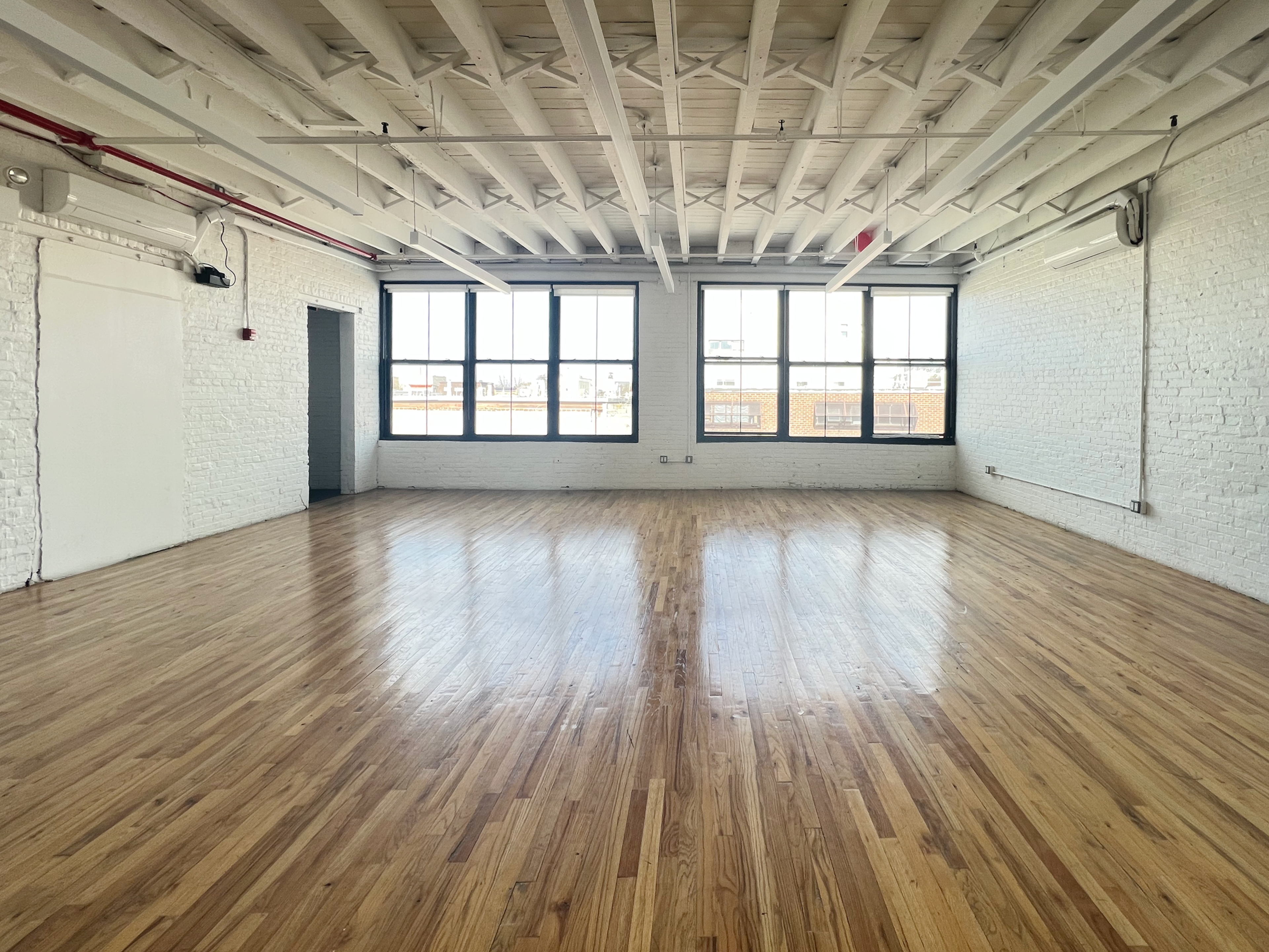 A spacious, empty room features hardwood flooring and large windows along one wall.