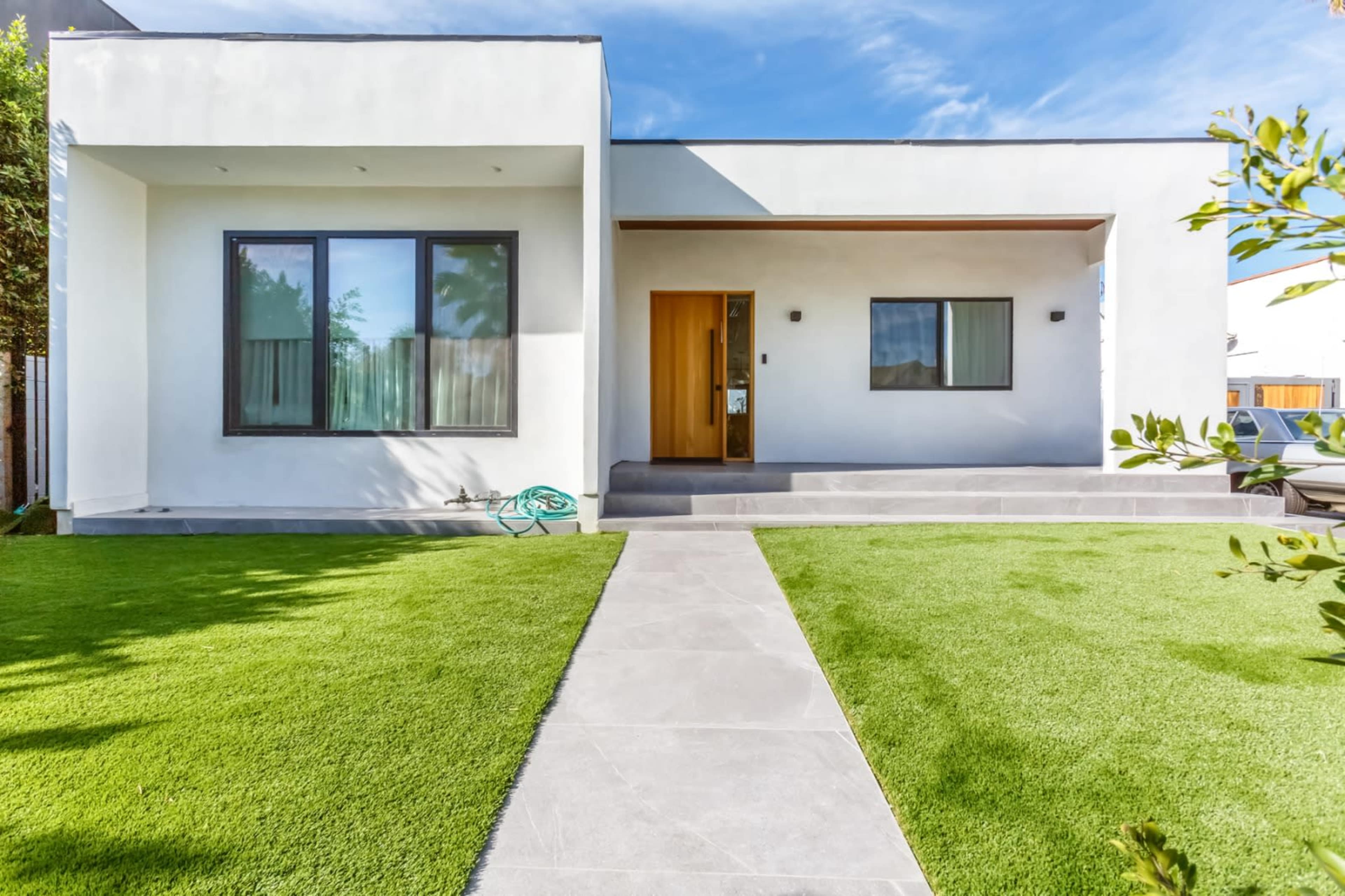 A modern white house with large windows and a stone pathway leading to the entrance, surrounded by green grass.