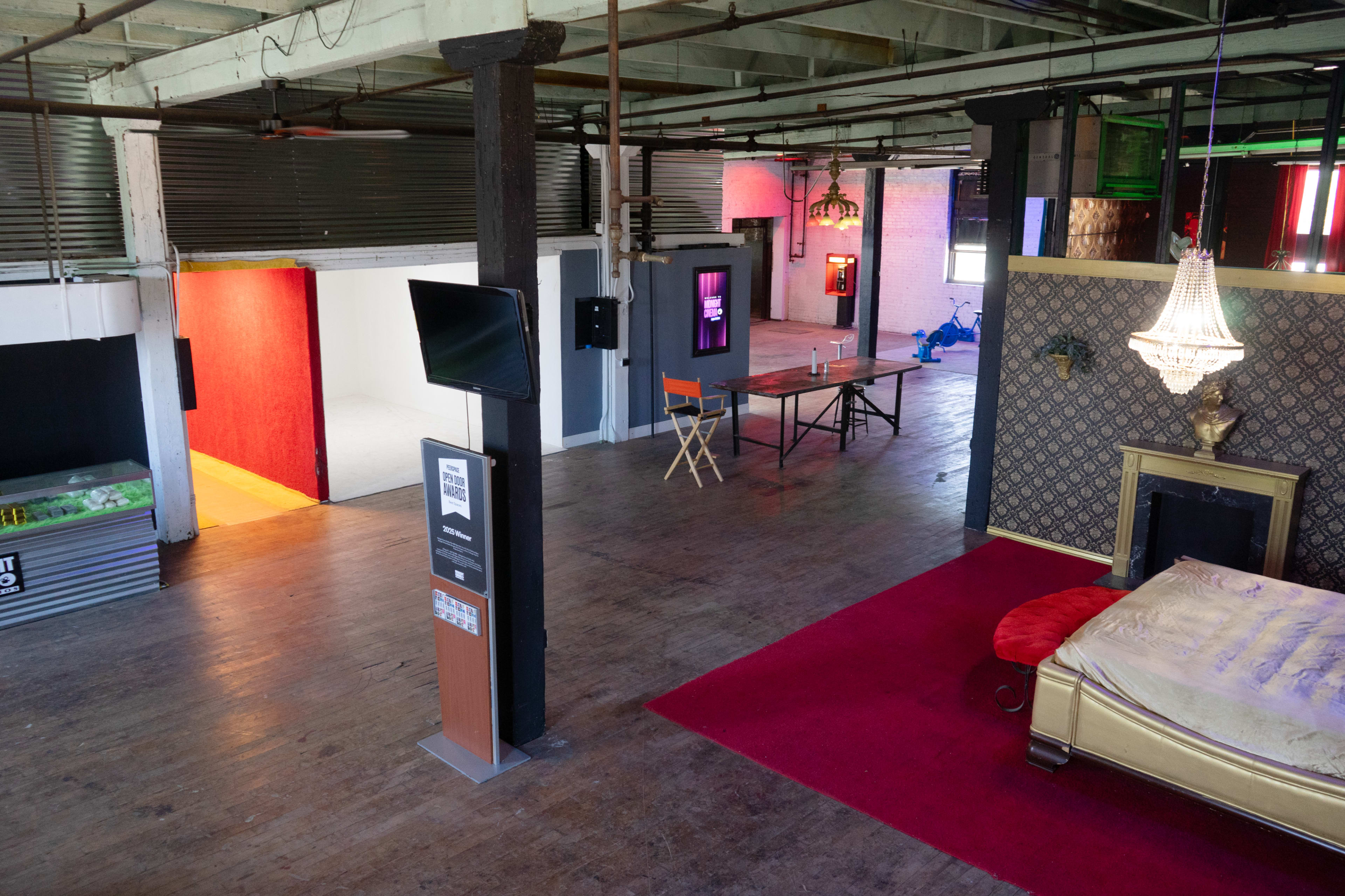 The image shows an open interior space featuring a gold bed on a red carpet, wooden floors, and areas with contrasting lighting and furniture arrangements.