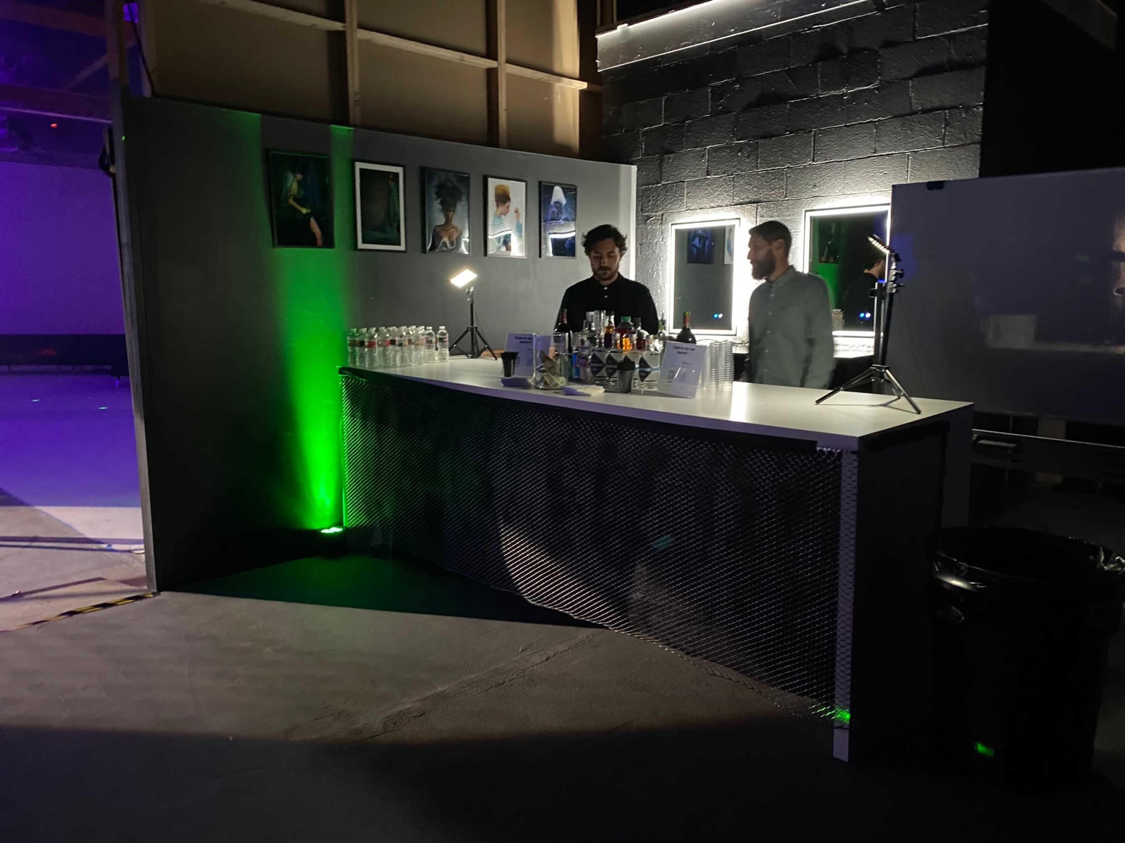 A bartender prepares drinks at a modern bar setup in a dimly lit event space.