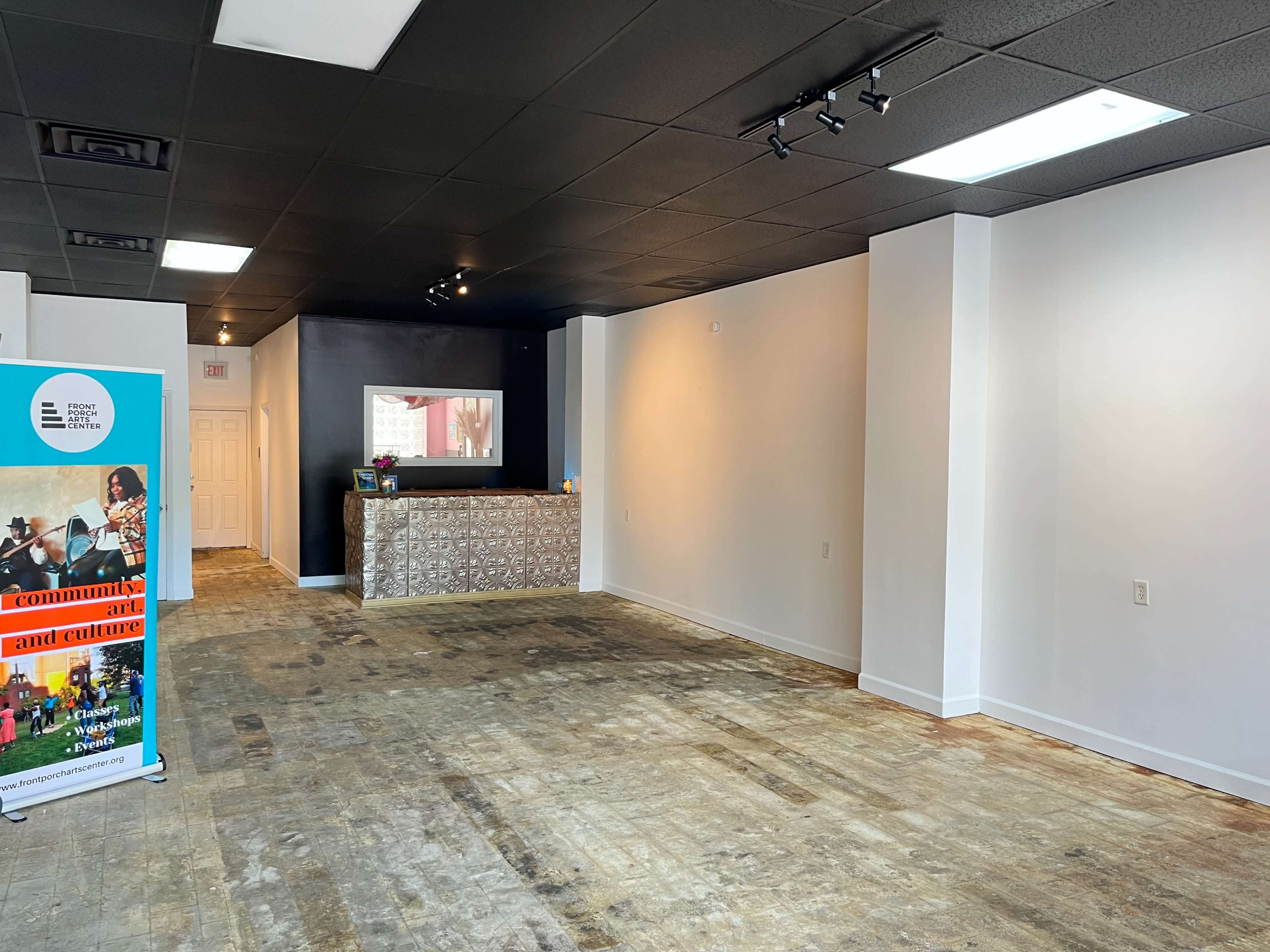 An empty room with a light-colored wall, a dark reception area with a countertop, and a display sign on the left side.