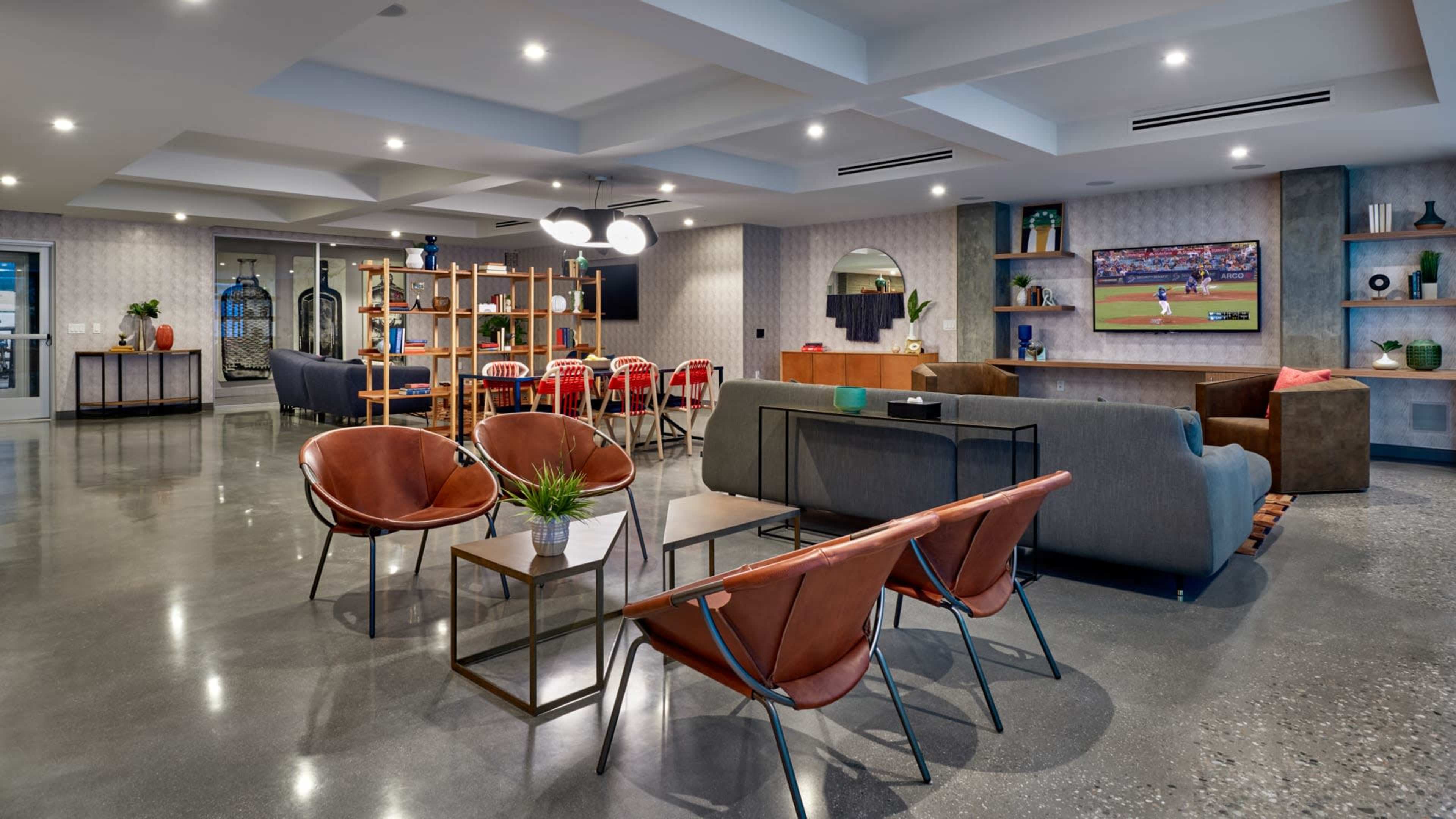 A modern living space with a mix of seating arrangements, a television mounted on the wall, and a dining area in the background.