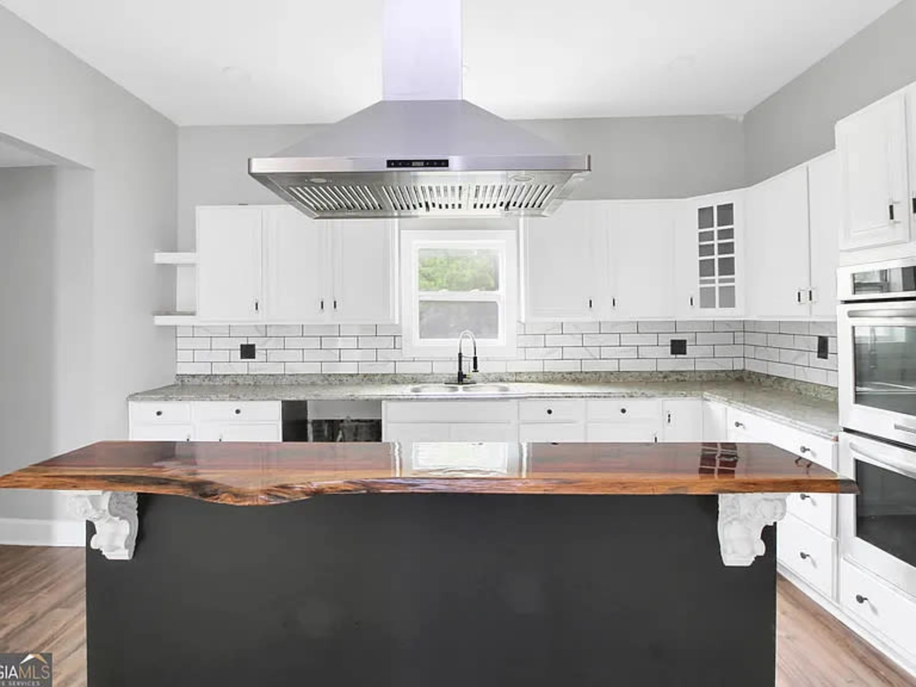 A modern kitchen features white cabinetry, a large island with a wooden countertop, and stainless steel appliances.